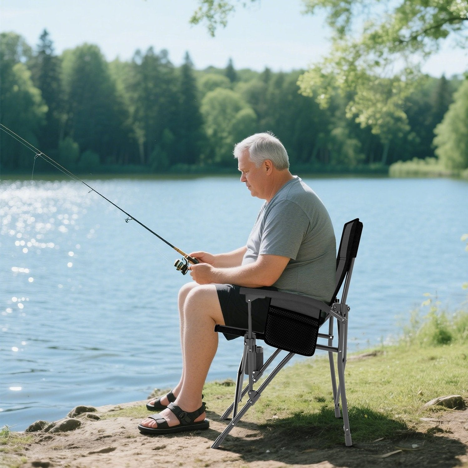 Un hombre mayor pesca sentado en una silla junto a un lago. Sostiene una caña de pescar. Árboles y agua son el fondo.