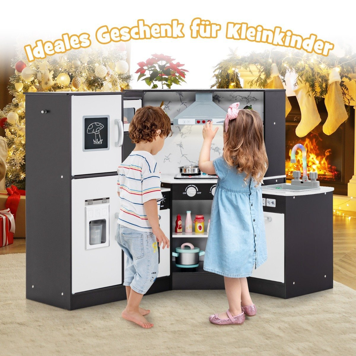 Dos niños juegan con una cocina de juguete. La cocina tiene nevera, estufa y fregadero. Decoraciones navideñas al fondo.