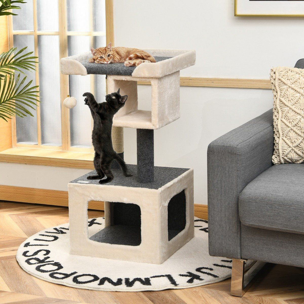Un gato negro está de pie en un árbol para gatos, alcanzando un juguete, mientras que un gato naranja descansa en el nivel superior.