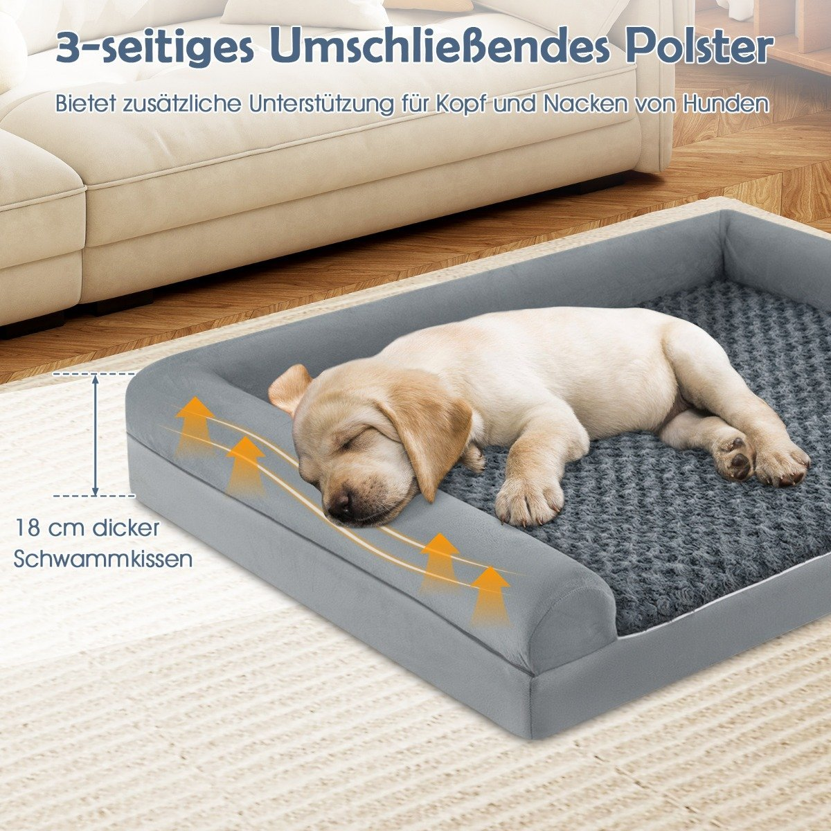Un cachorro dormido descansa en una cama para perros gris. La cama tiene un borde acolchado. El fondo muestra un sofá y texto en alemán.