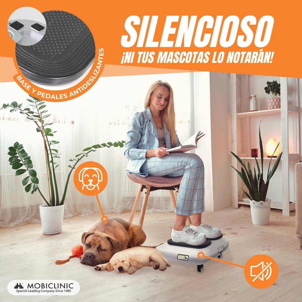 Una mujer lee de pie sobre una plataforma vibratoria. Dos perros descansan cerca. El fondo muestra plantas y una estantería.