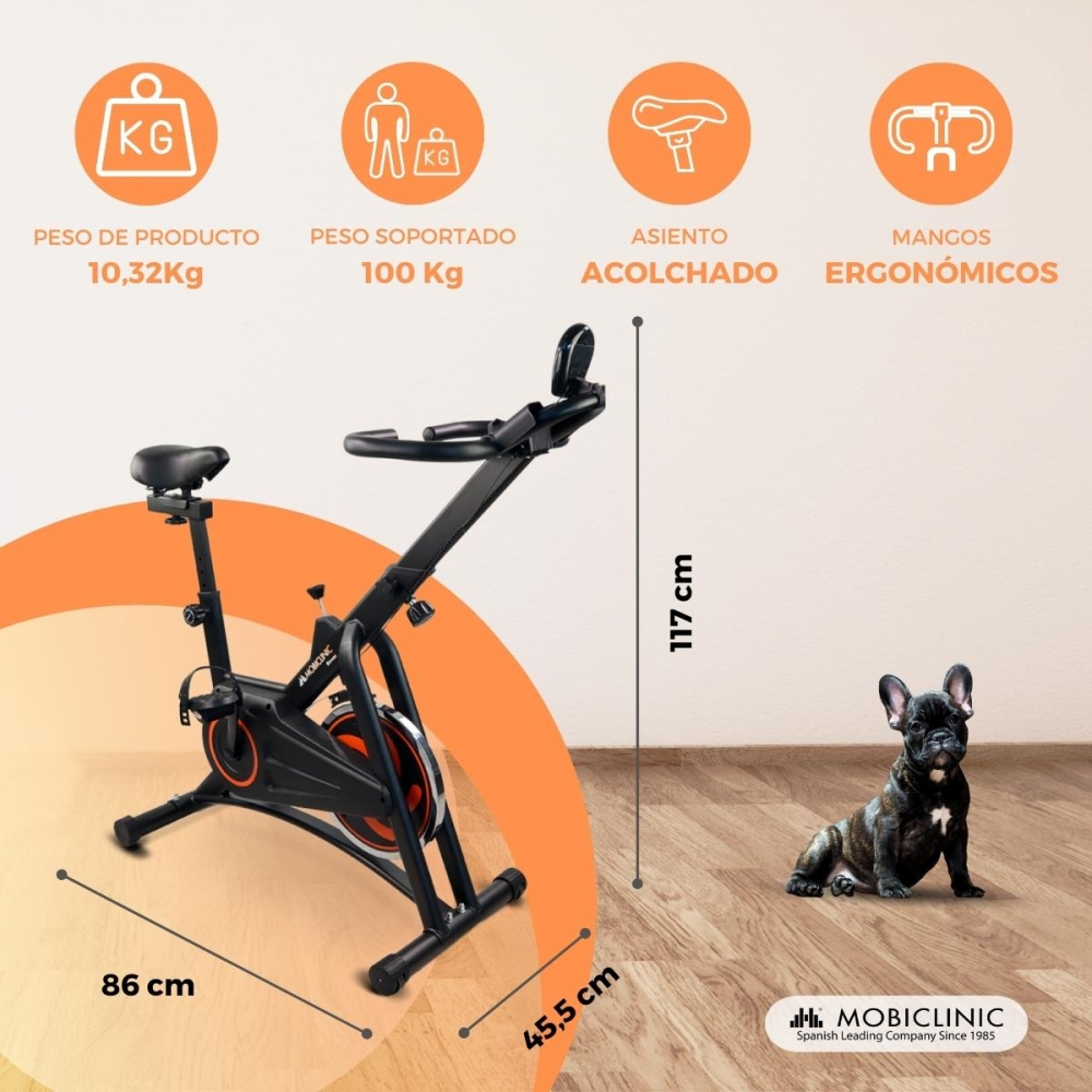 Una bicicleta estática negra con detalles naranjas. Un perro está cerca. El texto indica peso, dimensiones y características.