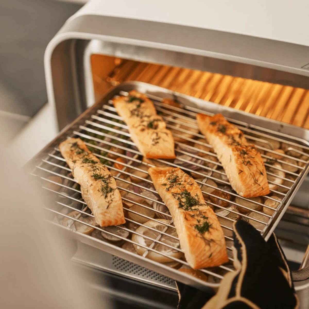 Vier gekochte Lachsfilets auf einem Metallrost im Ofen. Der Fisch ist goldbraun, mit Kräutern garniert und liegt über Gemüse.