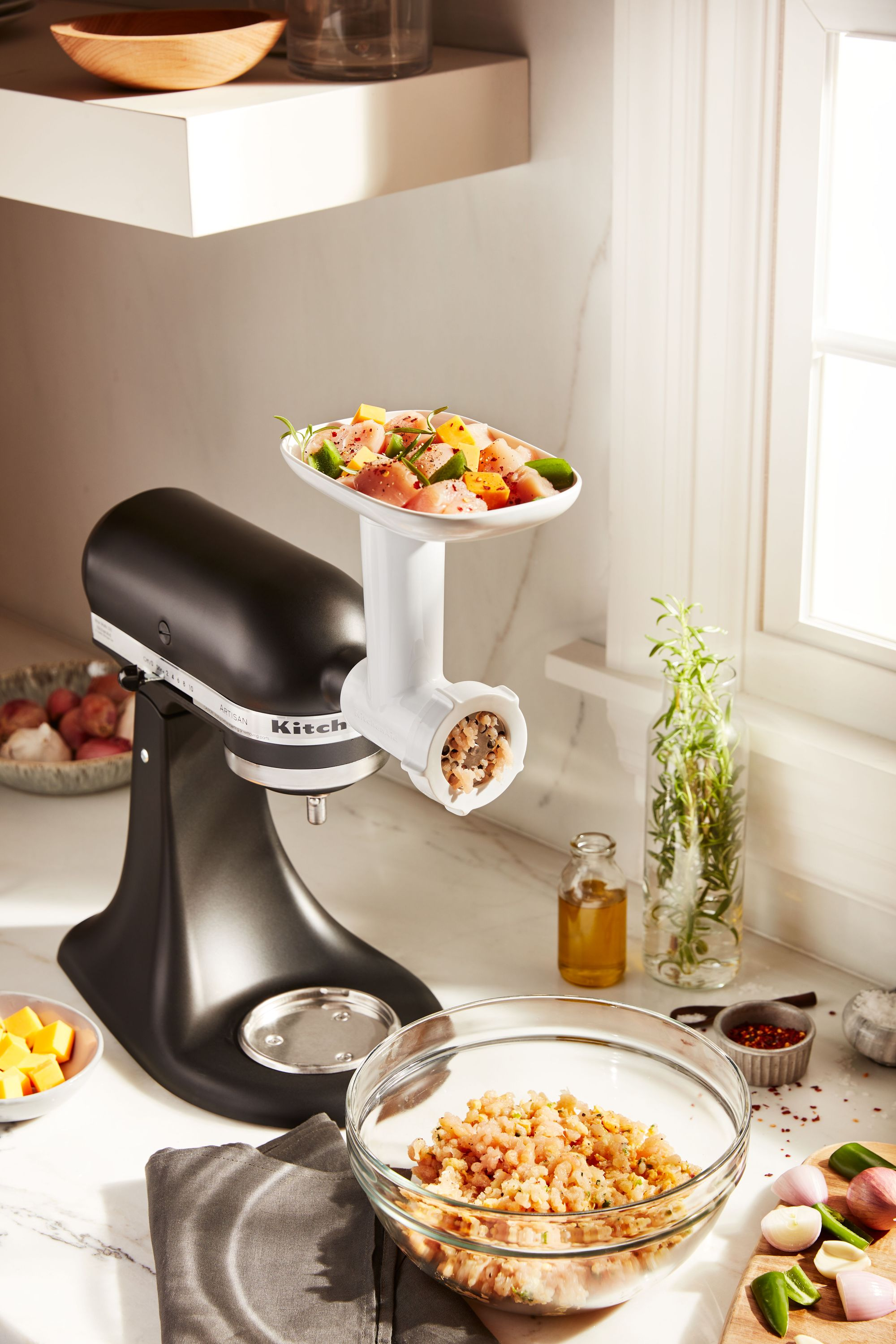 Ein schwarzer KitchenAid-Zerkleinerer zerkleinert Fleisch. Zutaten sind vorbereitet: Fleisch, Käse, Paprika und Gewürze.