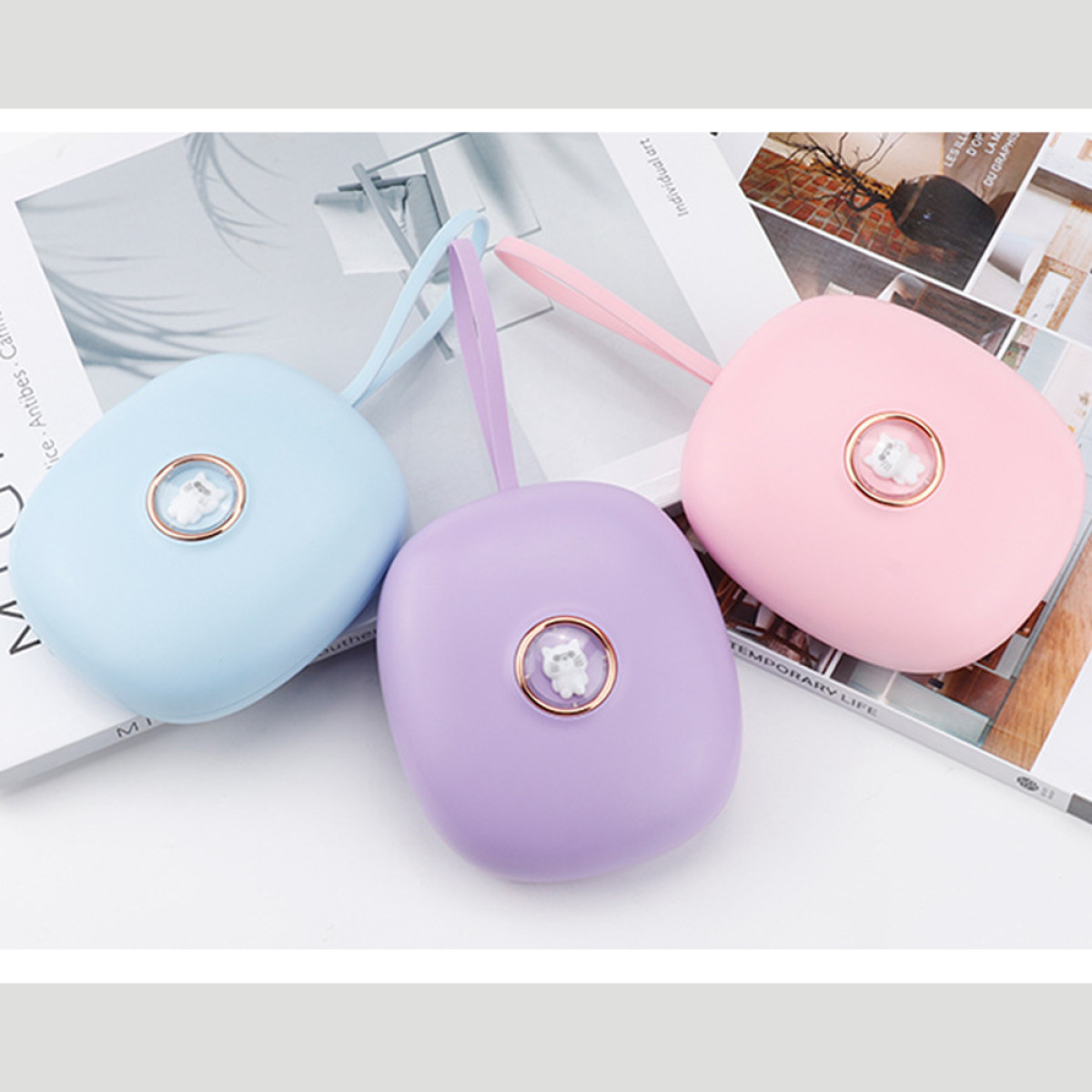 Trzy kolorowe, podręczne wentylatory: niebieski, fioletowy i różowy. Każdy ma małą dekorację w kształcie misia i pasek. Leżą na magazynach.