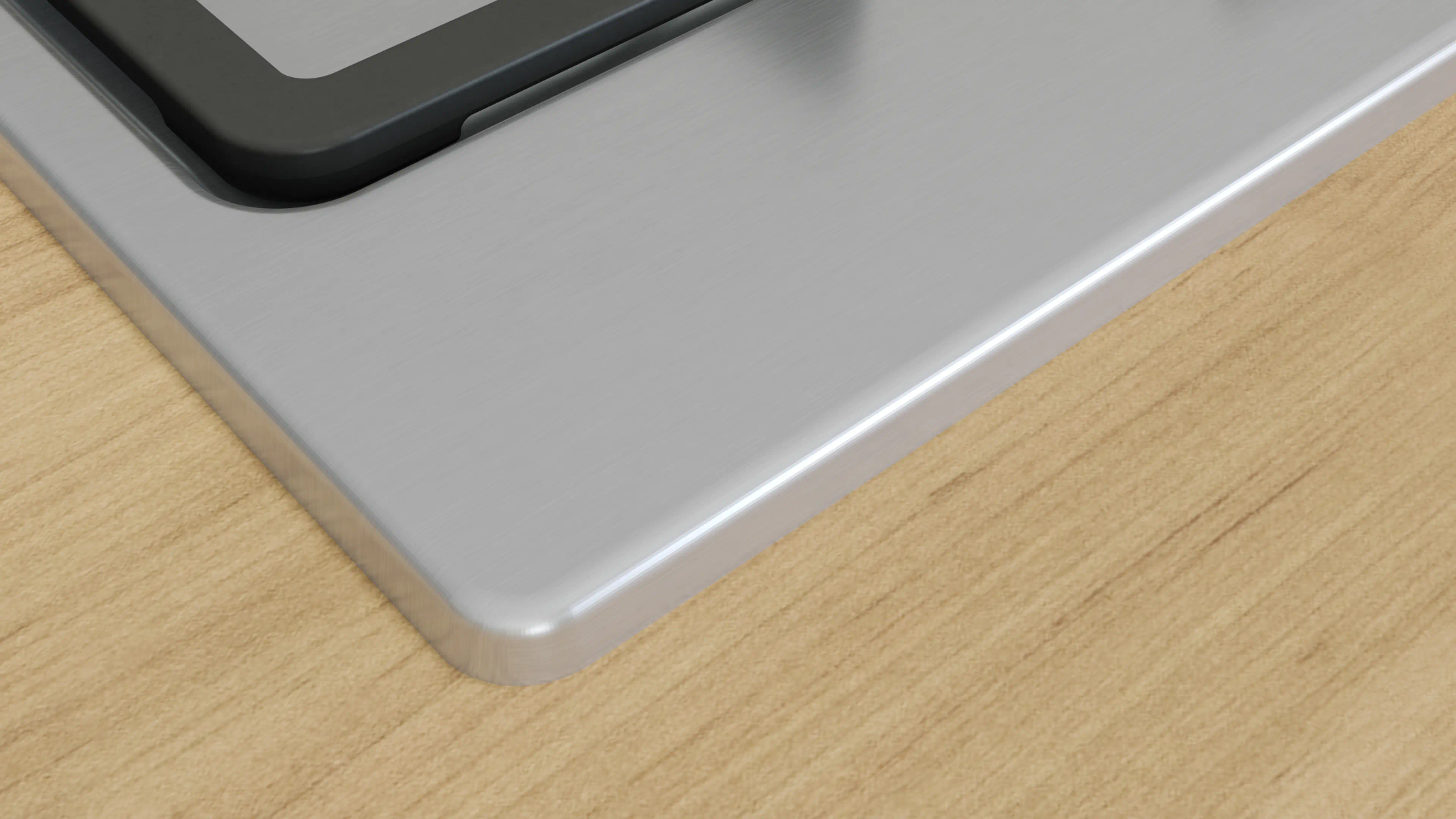 Zbliżenie szczotkowanej metalowej powierzchni z ciemną krawędzią. Leży na jasnym drewnianym stole. Kąt jest z góry.