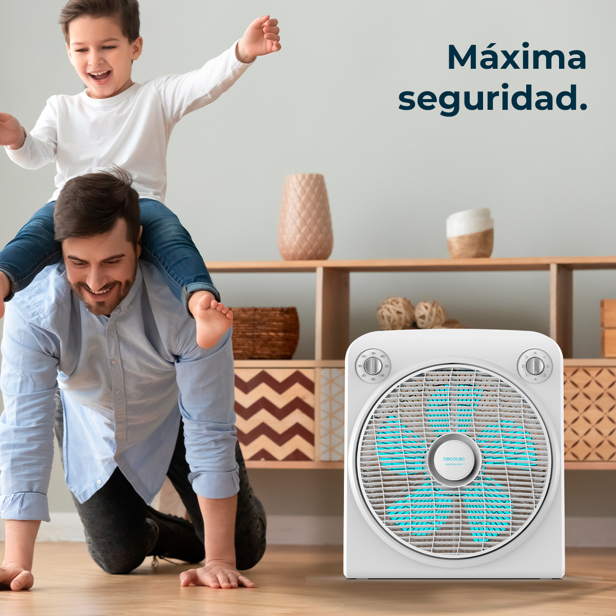 Mężczyzna czołga się, chłopiec jedzie na jego plecach. Wentylator jest na pierwszym planie. Tło pokazuje półki z dekoracjami.