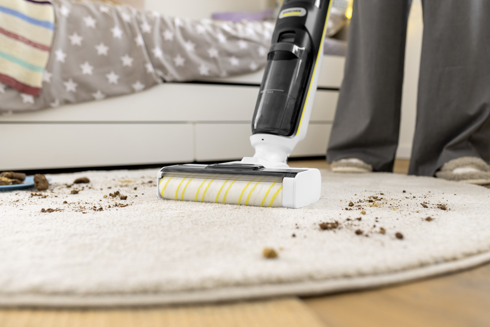 Een stofzuiger maakt een tapijt schoon met vuil. Een bed staat op de achtergrond. Een persoon stofzuigt het tapijt.