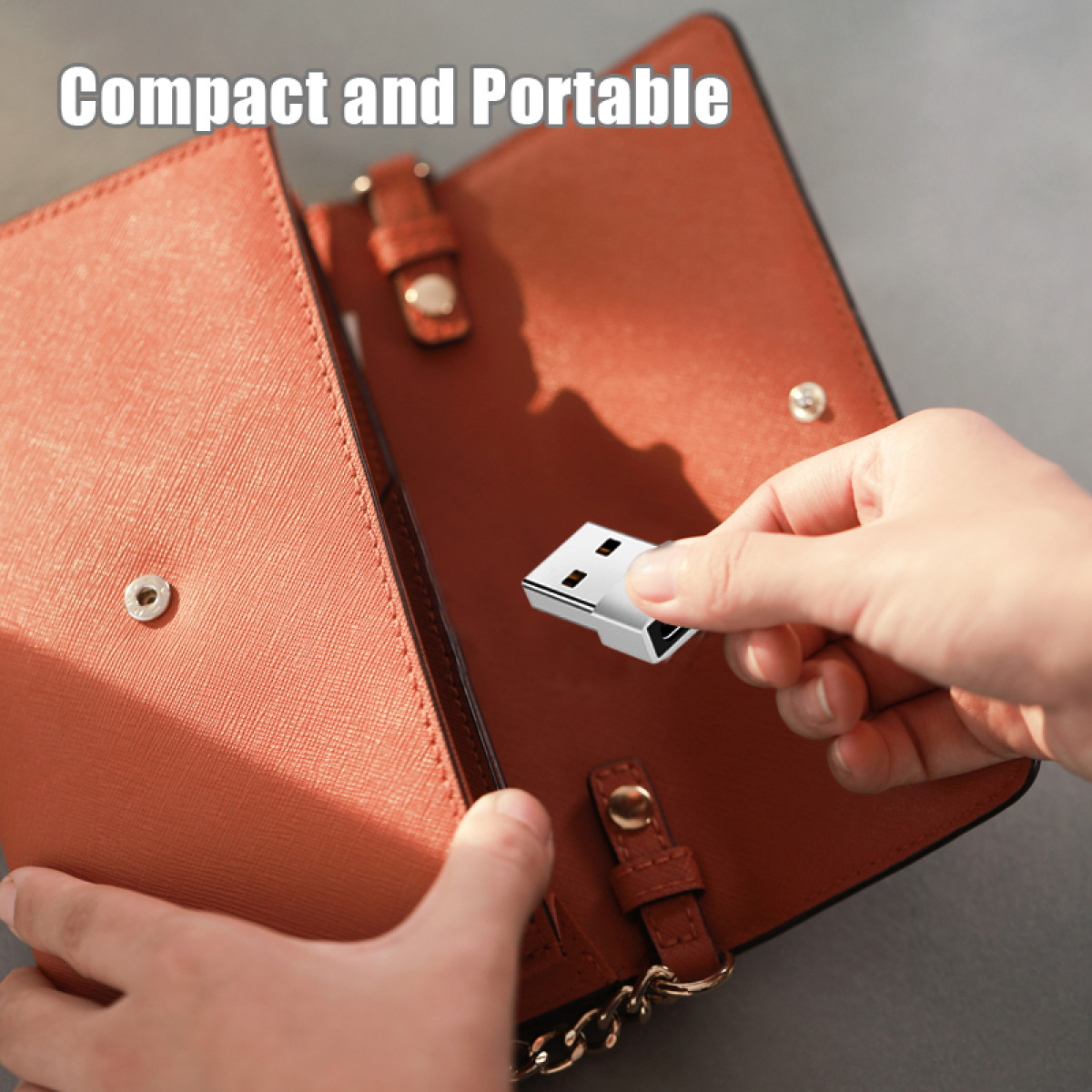 Ręka trzyma srebrny pendrive nad otwartym brązowym portfelem. Portfel leży na szarej powierzchni.