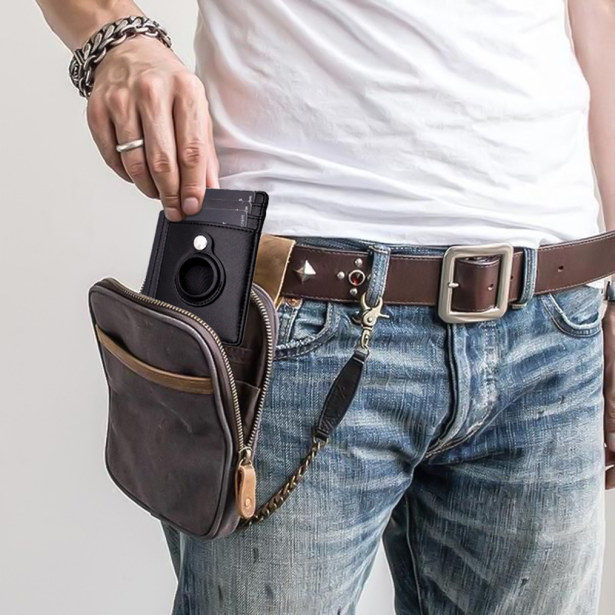 Eine Person hält eine schwarze Brieftasche, mit einer am Gürtel befestigten Tasche. Sie tragen ein weißes Hemd und blaue Jeans.