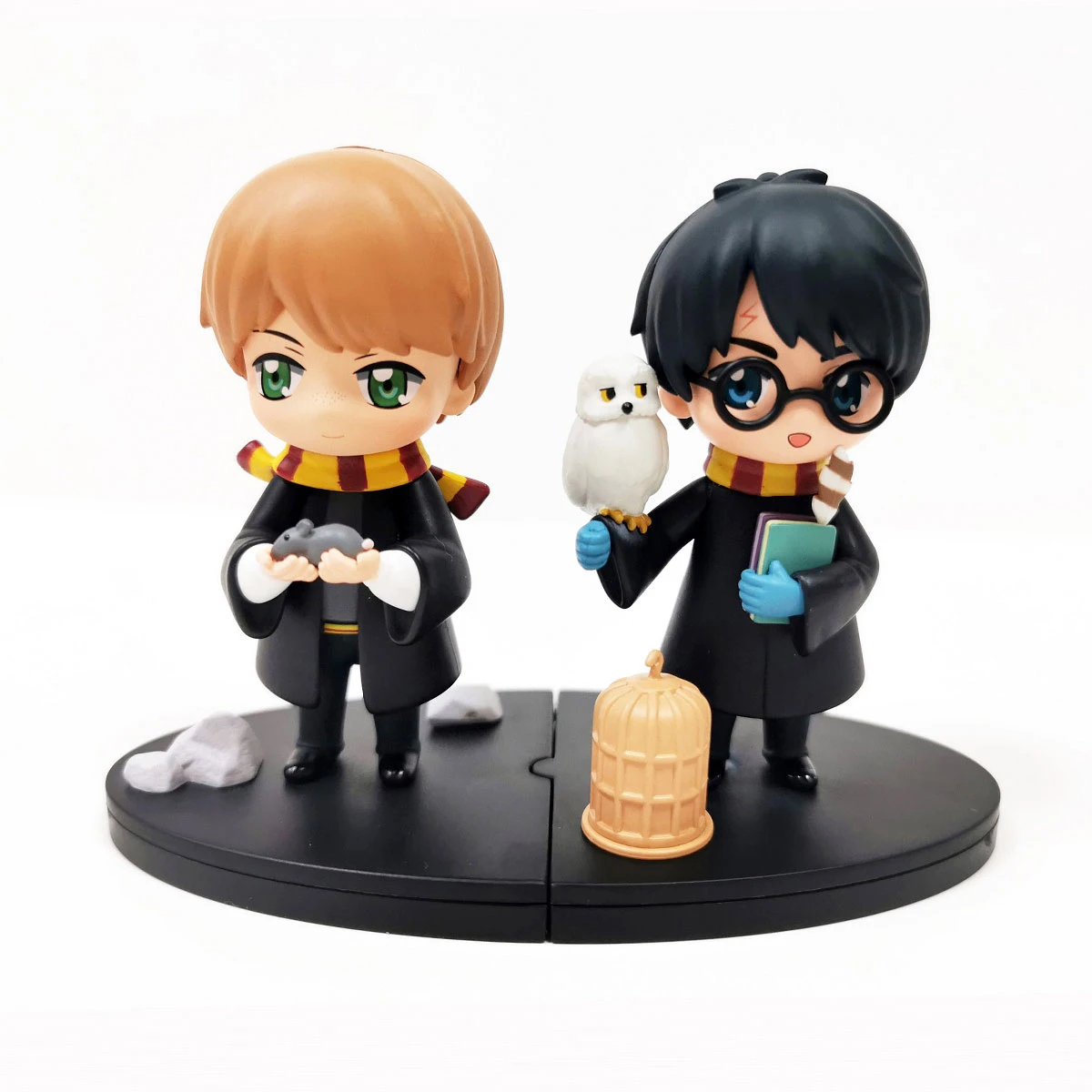 Dos figuras de Harry Potter: Ron con una rata, Harry con lechuza, gafas y libro. Ambos visten túnicas y bufandas de Hogwarts.