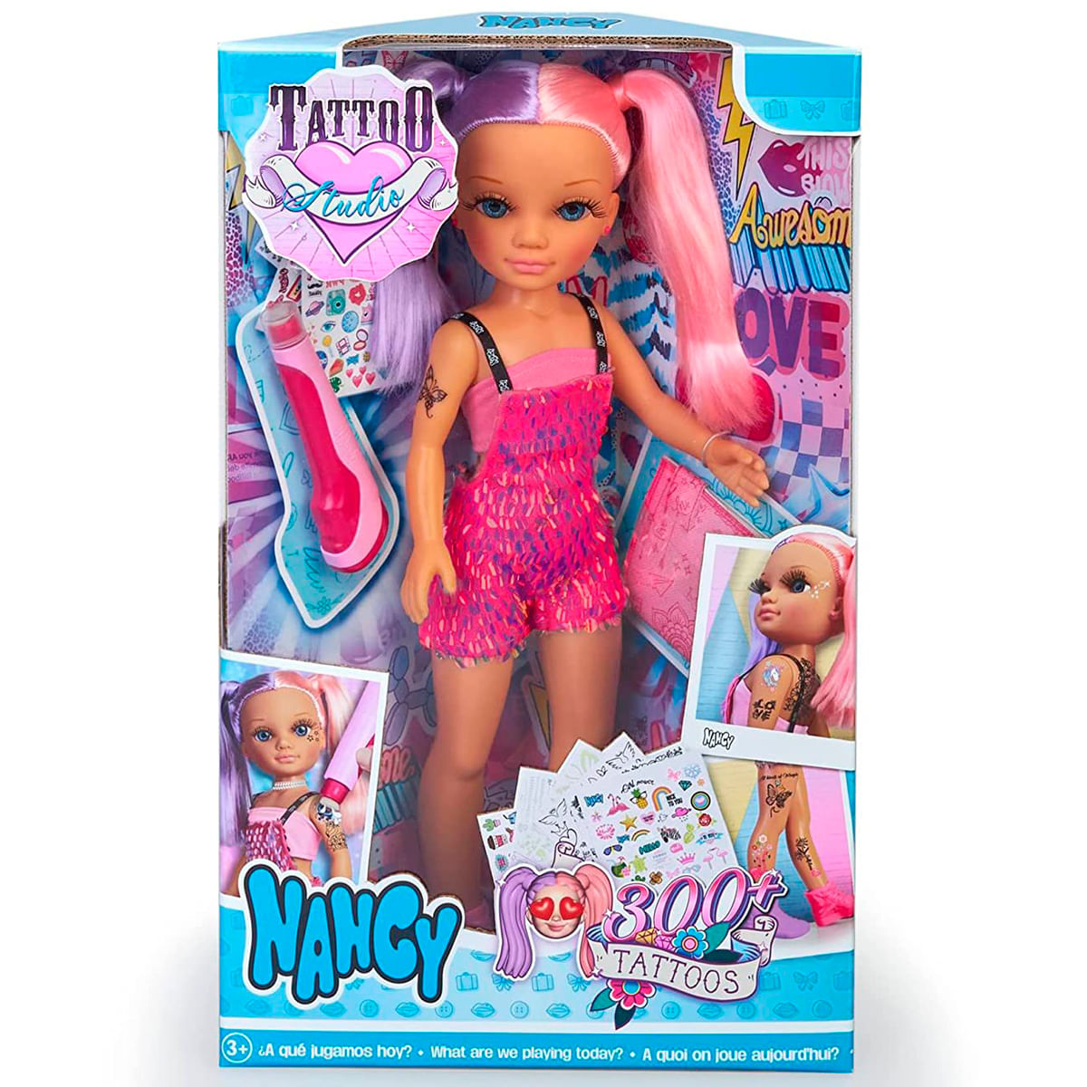 Una muñeca Nancy en una caja. Tiene el pelo rosa y morado y lleva un conjunto rosa. La caja dice 'Tattoo Studio' y '300 tatuajes'.