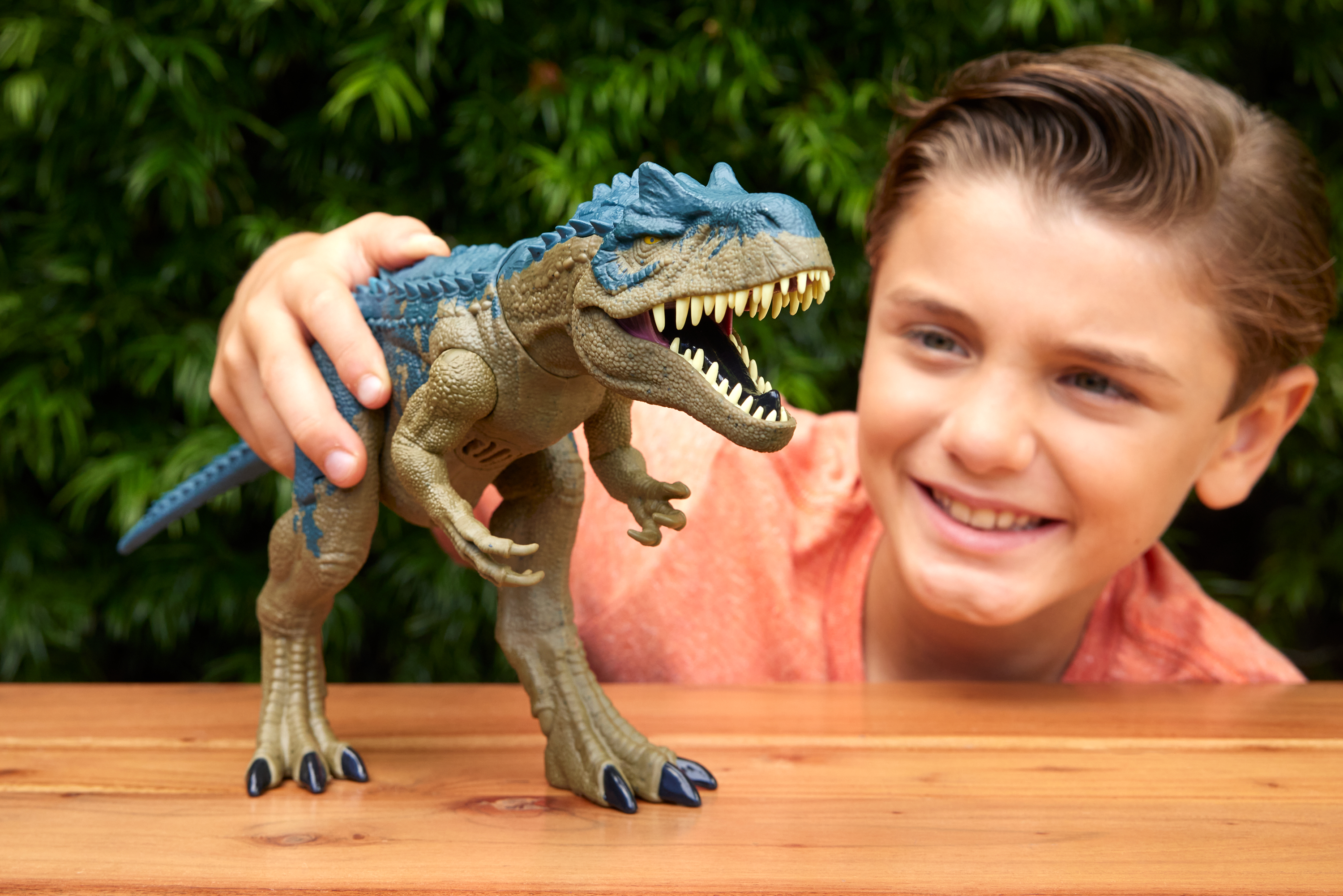 Un niño sostiene un juguete de dinosaurio. El juguete es marrón y azul. El niño sonríe.