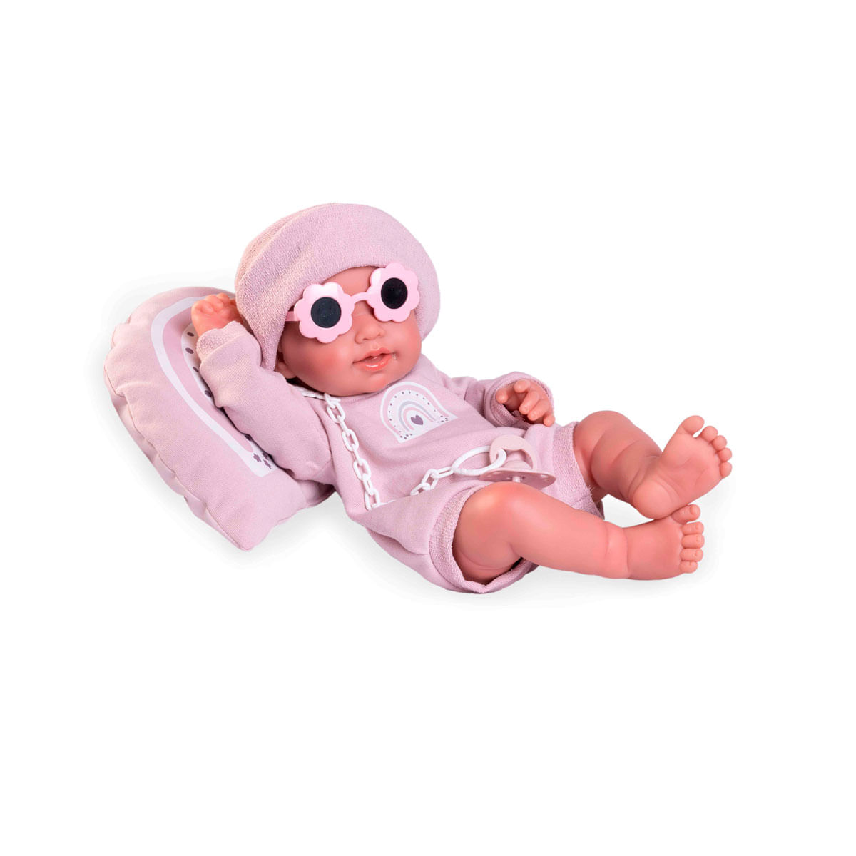 Una muñeca con gafas de sol rosas, gorro y atuendo está acostada sobre una almohada. Se adjunta un chupete. La muñeca está sobre un fondo blanco.