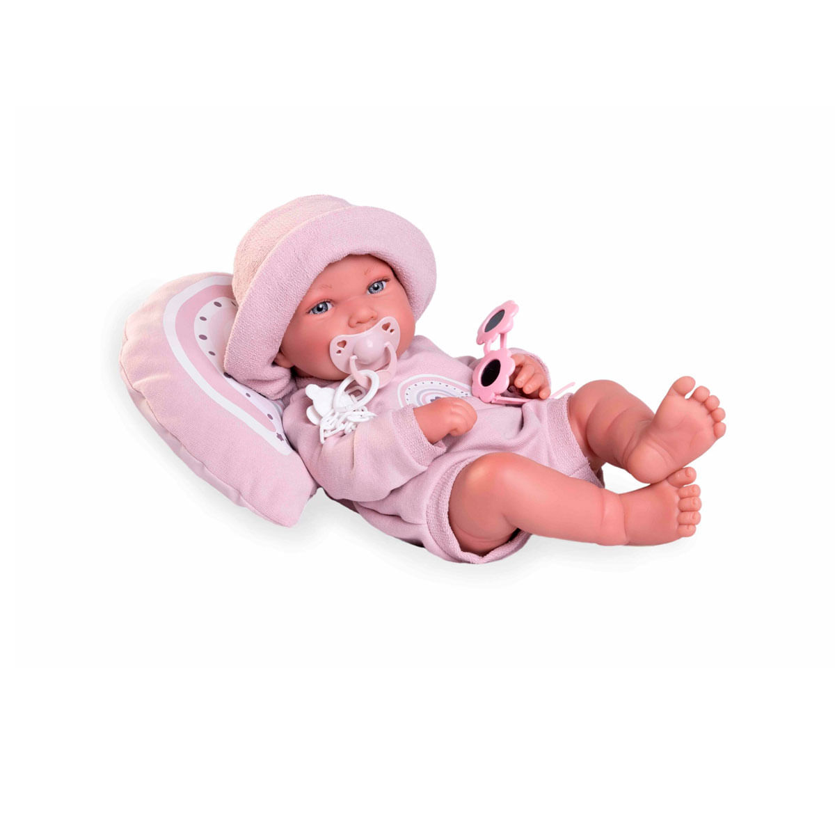 Una muñeca bebé con ropa rosa yace sobre una almohada rosa. Lleva un sombrero, tiene un chupete y sostiene gafas de sol. El fondo es blanco.