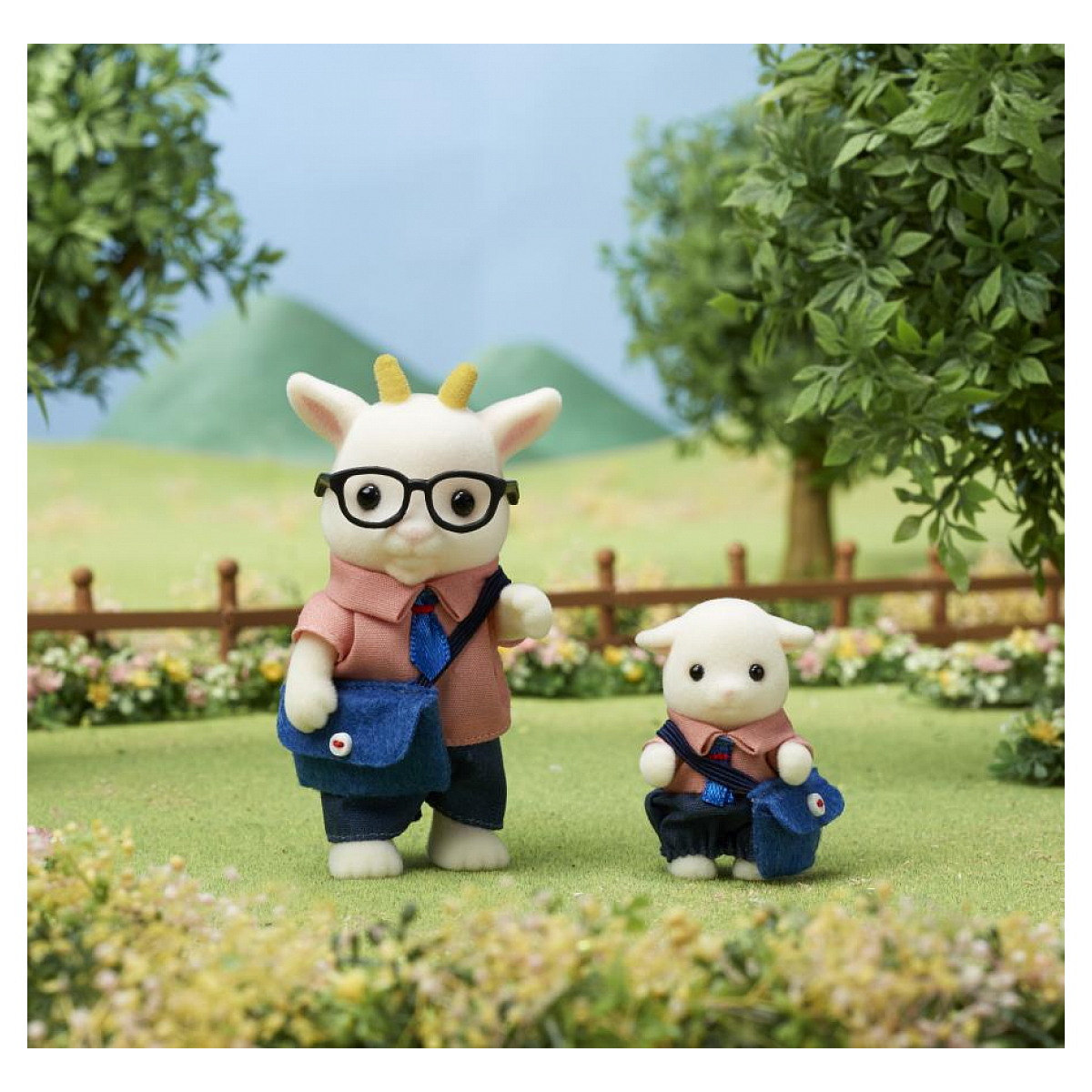 Dos figuras de cabra, una de pie con gafas, camisa y bolso. La otra más pequeña, también vestida de forma similar. Hierba verde y árboles al fondo.