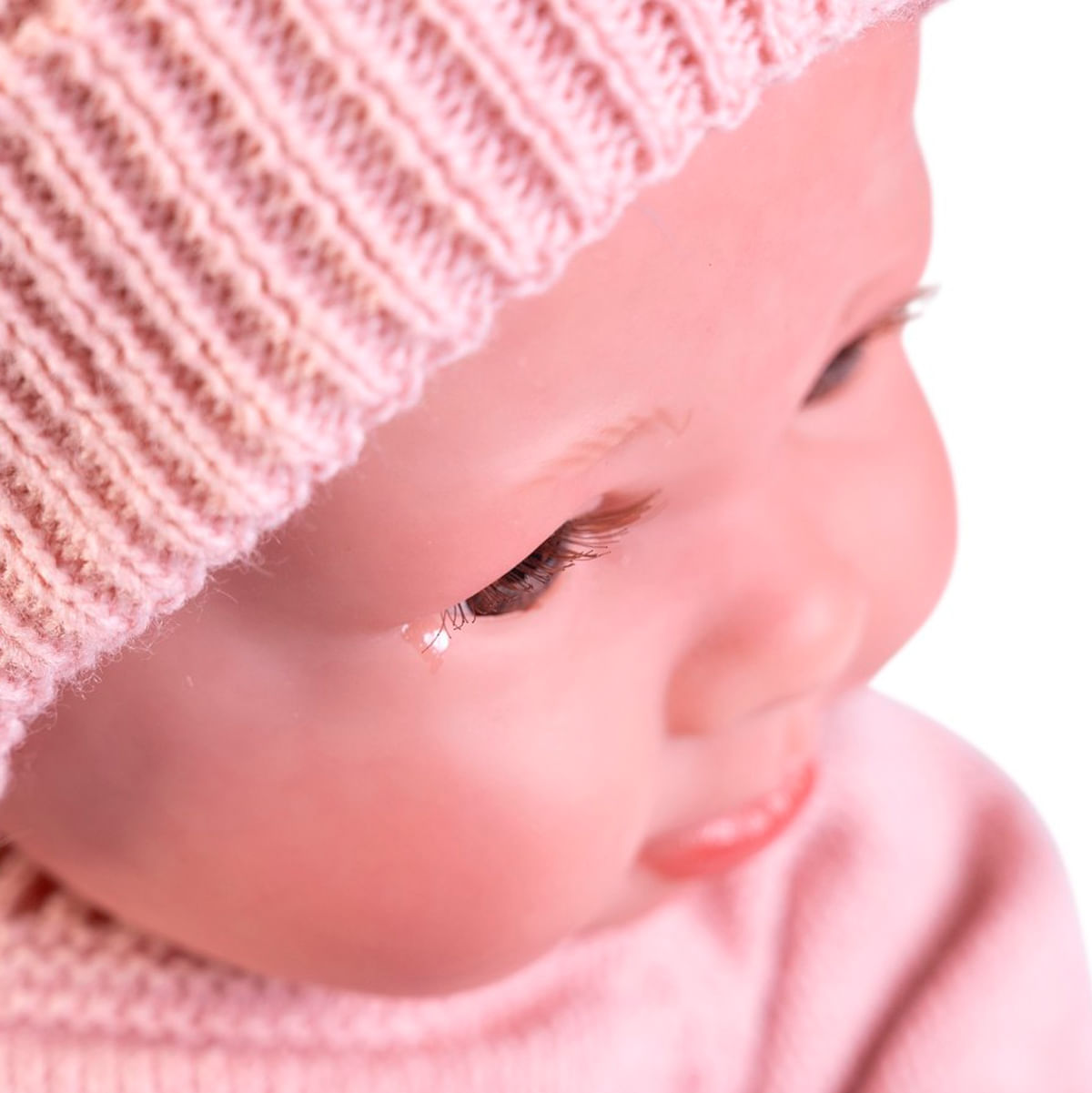 Primer plano de la cara de una muñeca con un gorro de punto rosa. La muñeca tiene ojos marrones y se ve una lágrima. Es una foto de estudio.