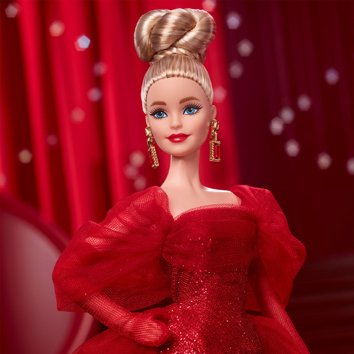 Una muñeca Barbie con un vestido rojo y cabello rubio recogido. Lleva aretes dorados y lápiz labial rojo sobre un fondo rojo.