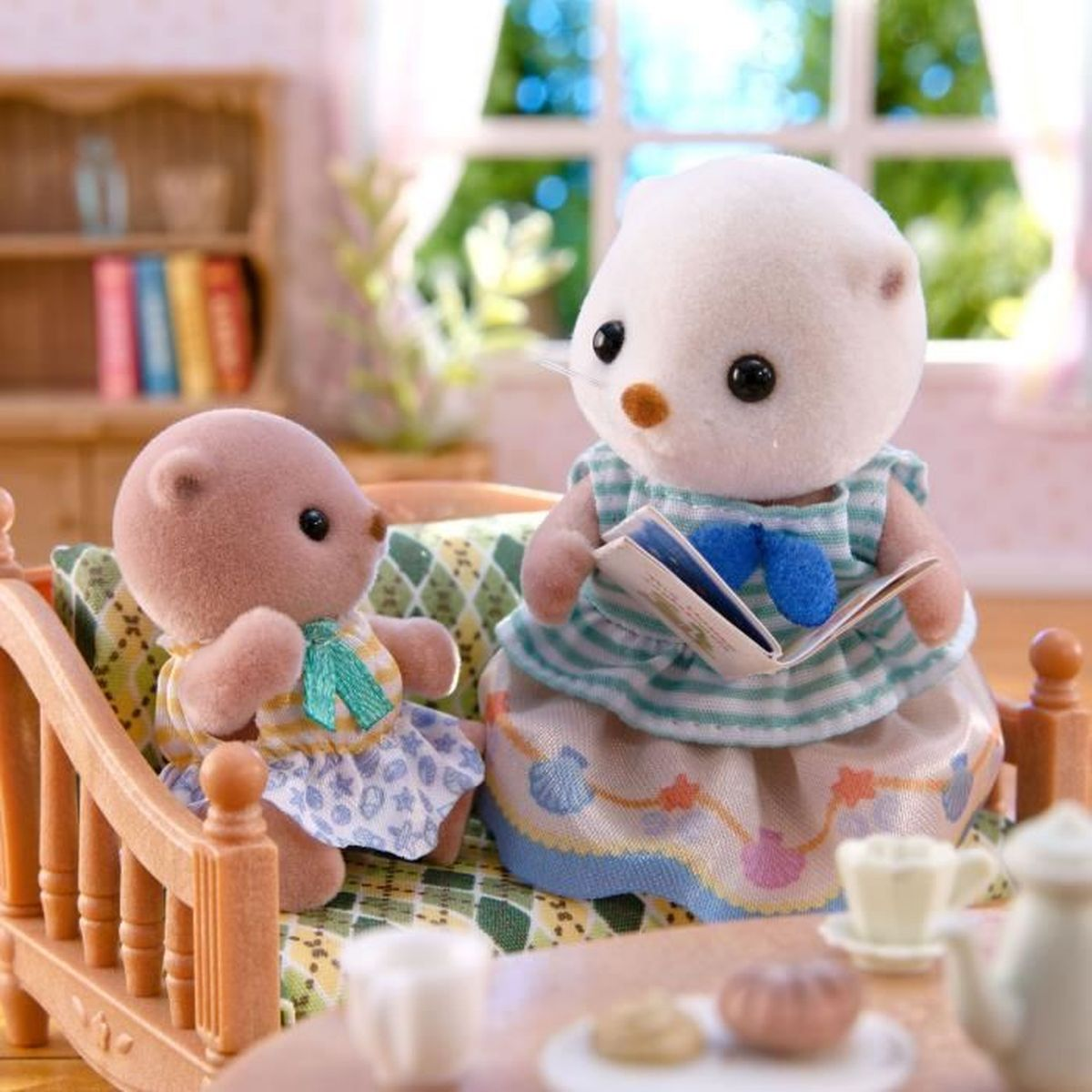 Dos figuras de animales en un sofá, una leyendo. Librería y ventana al fondo. Mesa con juego de té delante.