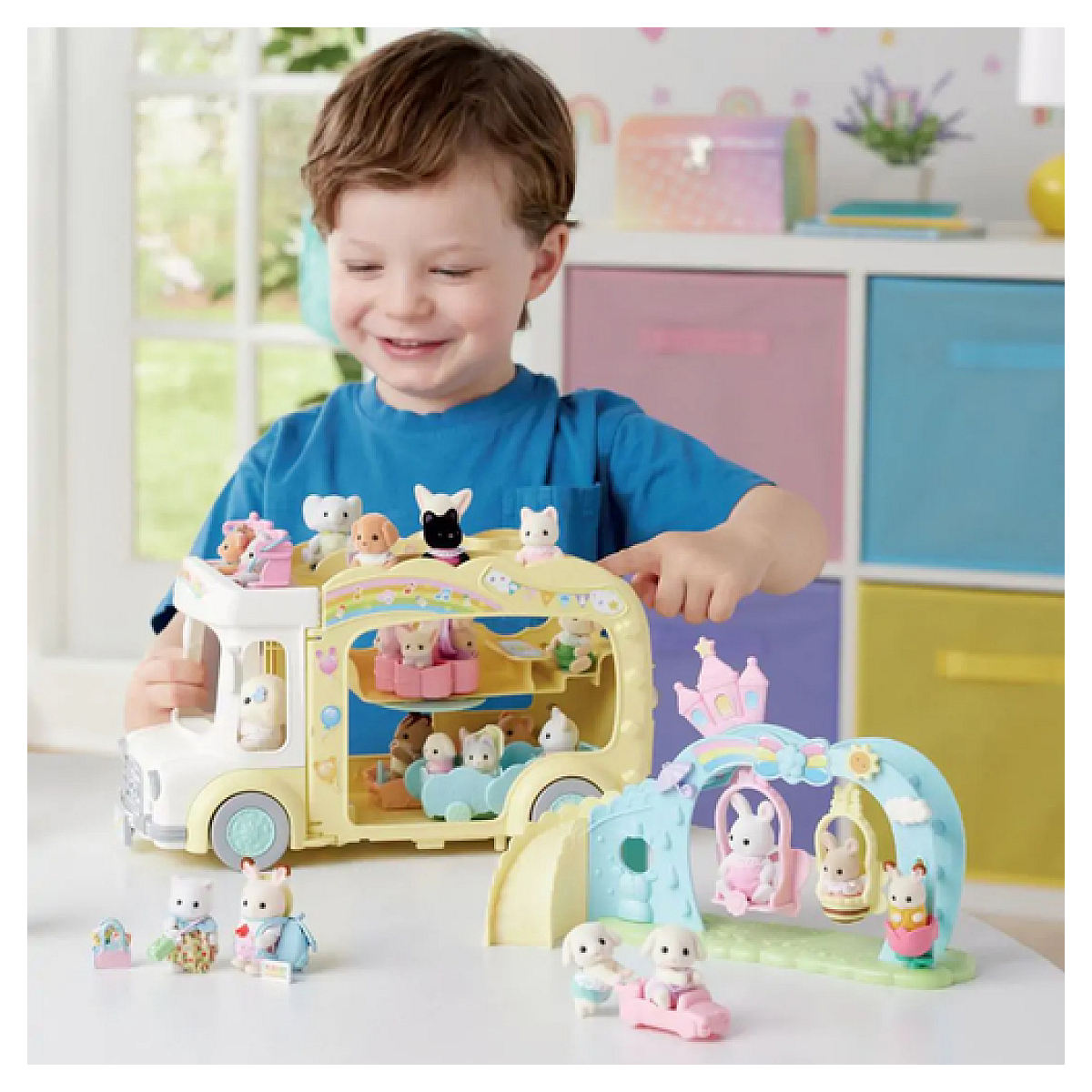 Un niño sonríe, jugando con un autobús de juguete lleno de figuras de animales y un columpio. Los juguetes están sobre una mesa.