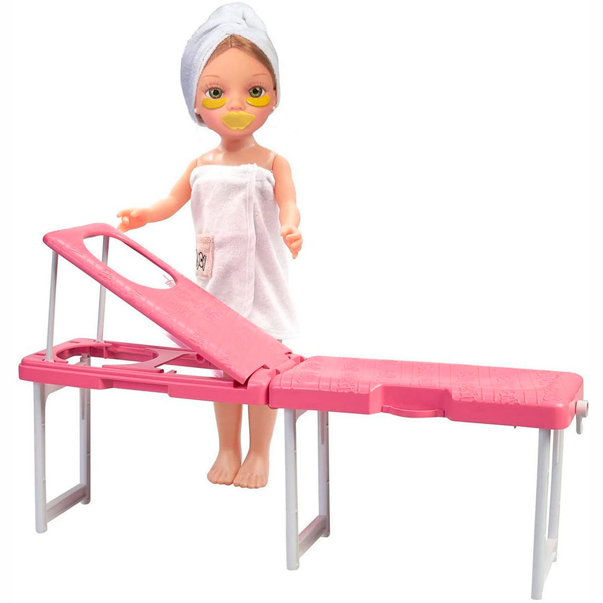 Una muñeca con una toalla y parches para los ojos está de pie cerca de una camilla de masaje rosa. La muñeca tiene una toalla en la cabeza.