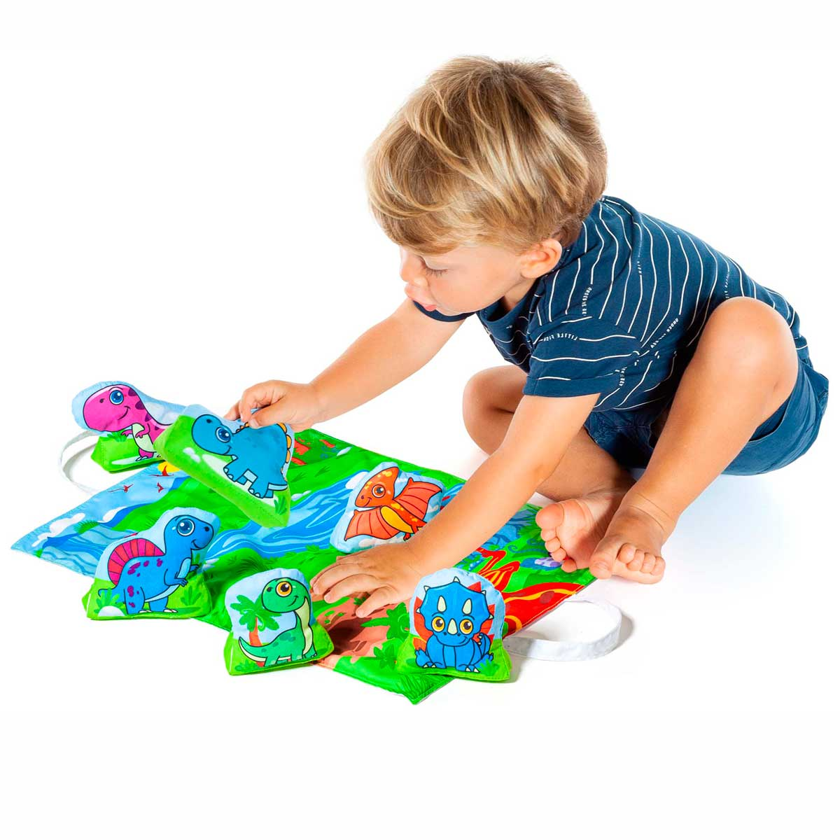 Un niño pequeño juega con juguetes con forma de dinosaurio en una estera. La estera representa un paisaje con agua y hierba. Lleva una camisa azul.