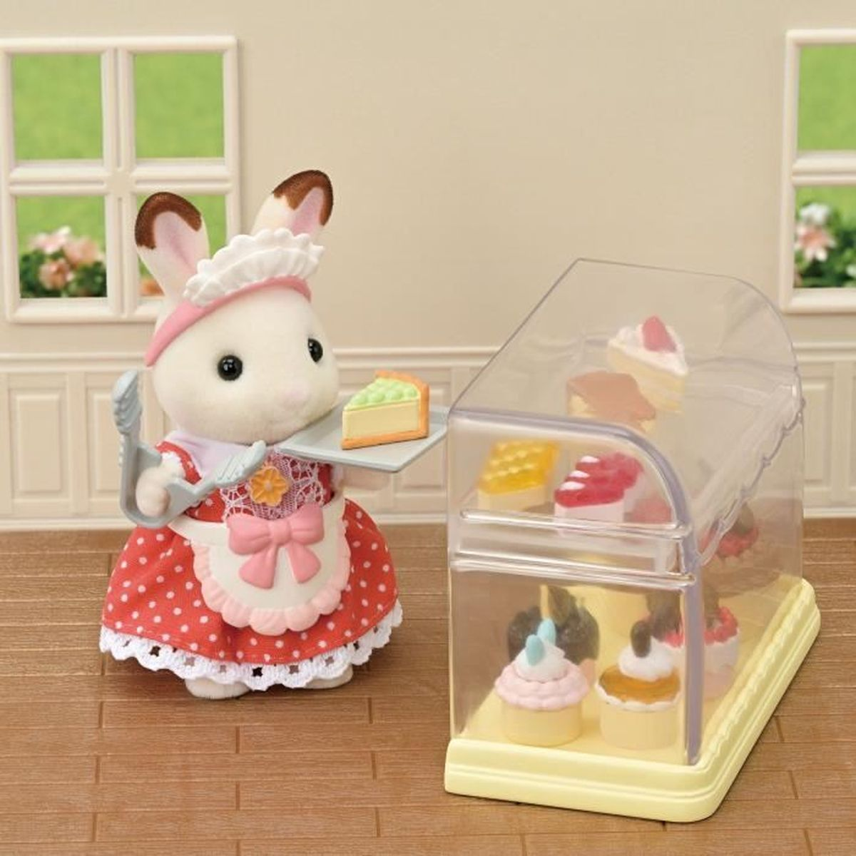 Una figura de conejo con un vestido de lunares rojos lleva una rebanada de pastel. Una vitrina con pasteles está a su lado en una panadería.
