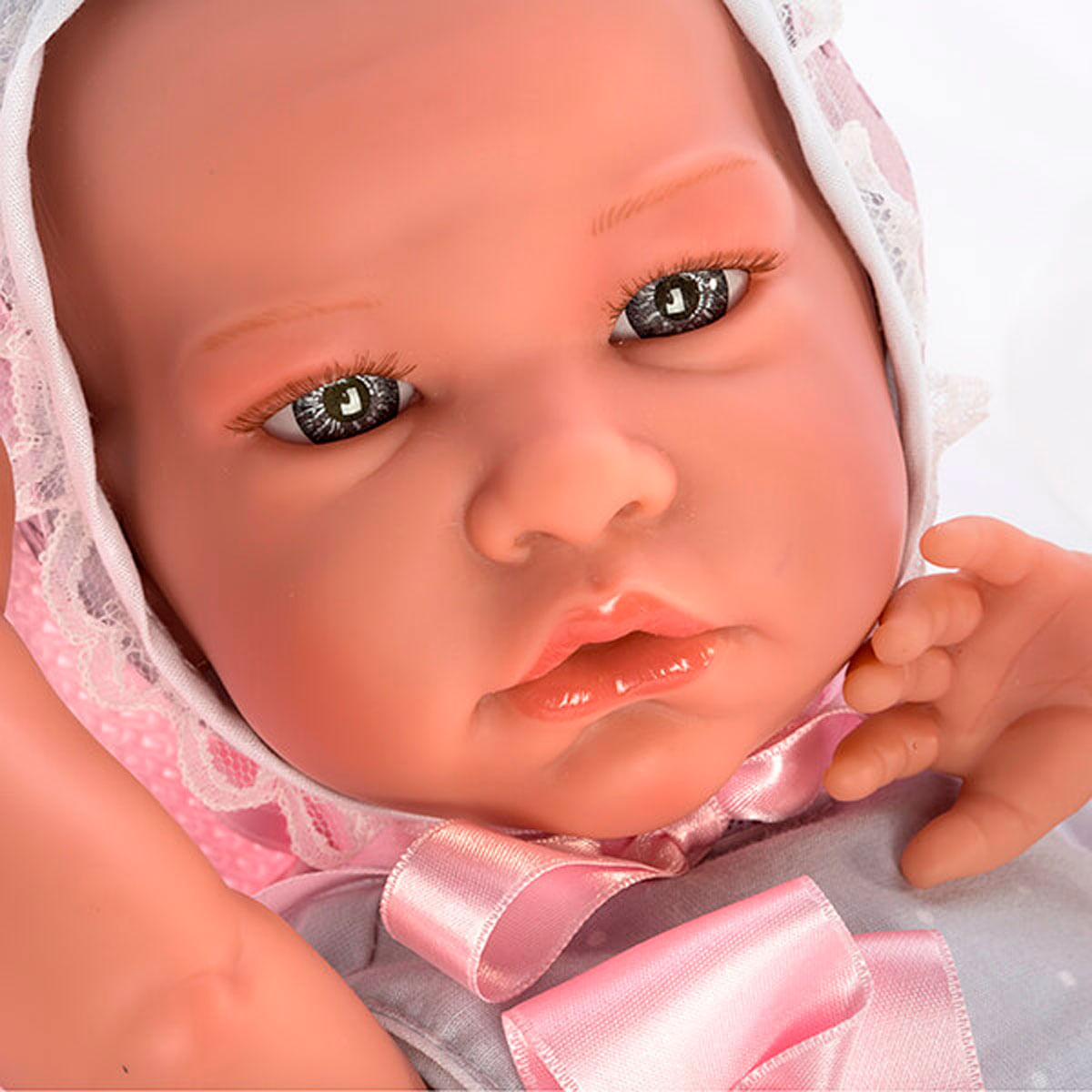 Primer plano de la cara de una muñeca. Tiene ojos grises, labios rosas y una cinta rosa. La muñeca lleva un gorro y un vestido gris.