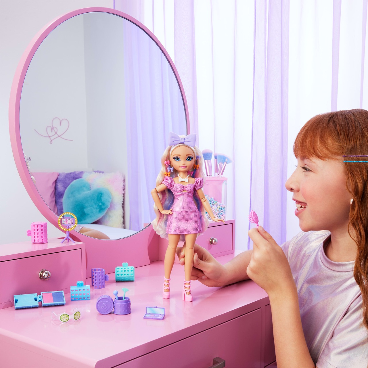 Una niña mira una muñeca en una mesa rosa. La muñeca tiene un vestido rosa y accesorios. Un espejo y herramientas de maquillaje están en el fondo.