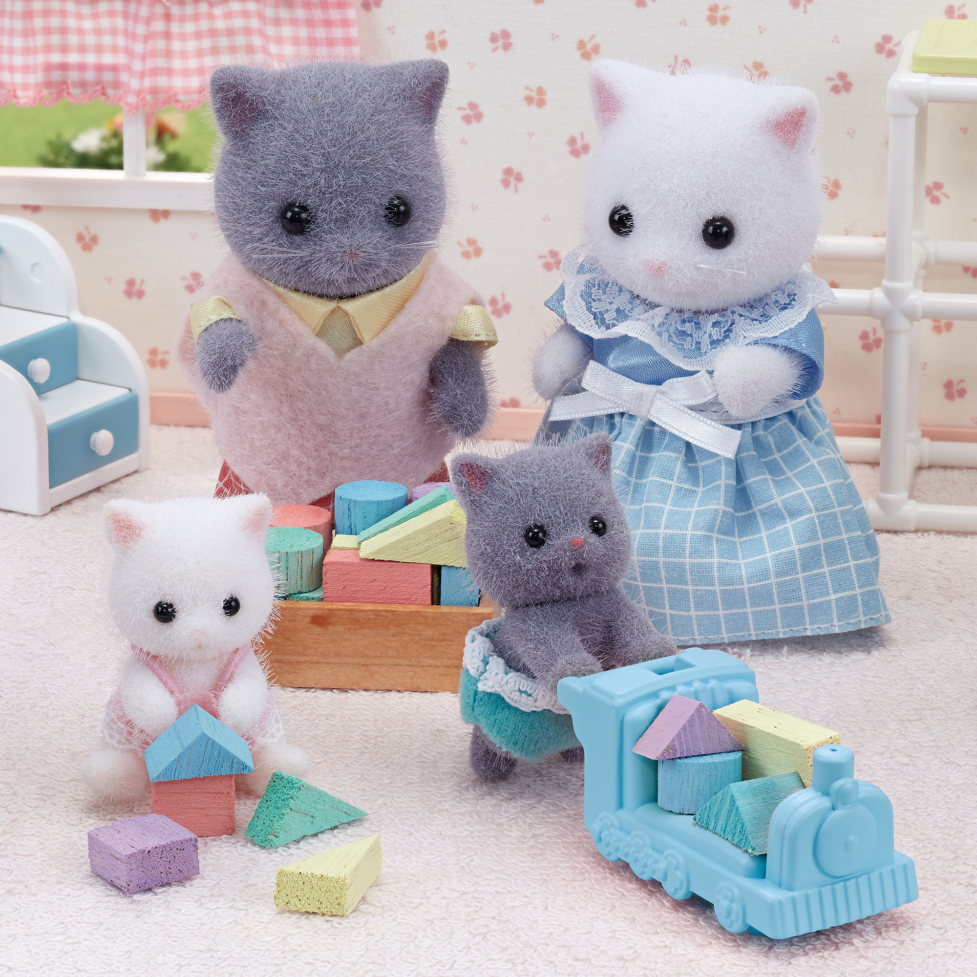 Cuatro figuras de gatos con bloques de juguete y un tren. Los gatos llevan ropa. Los bloques son de varios colores.