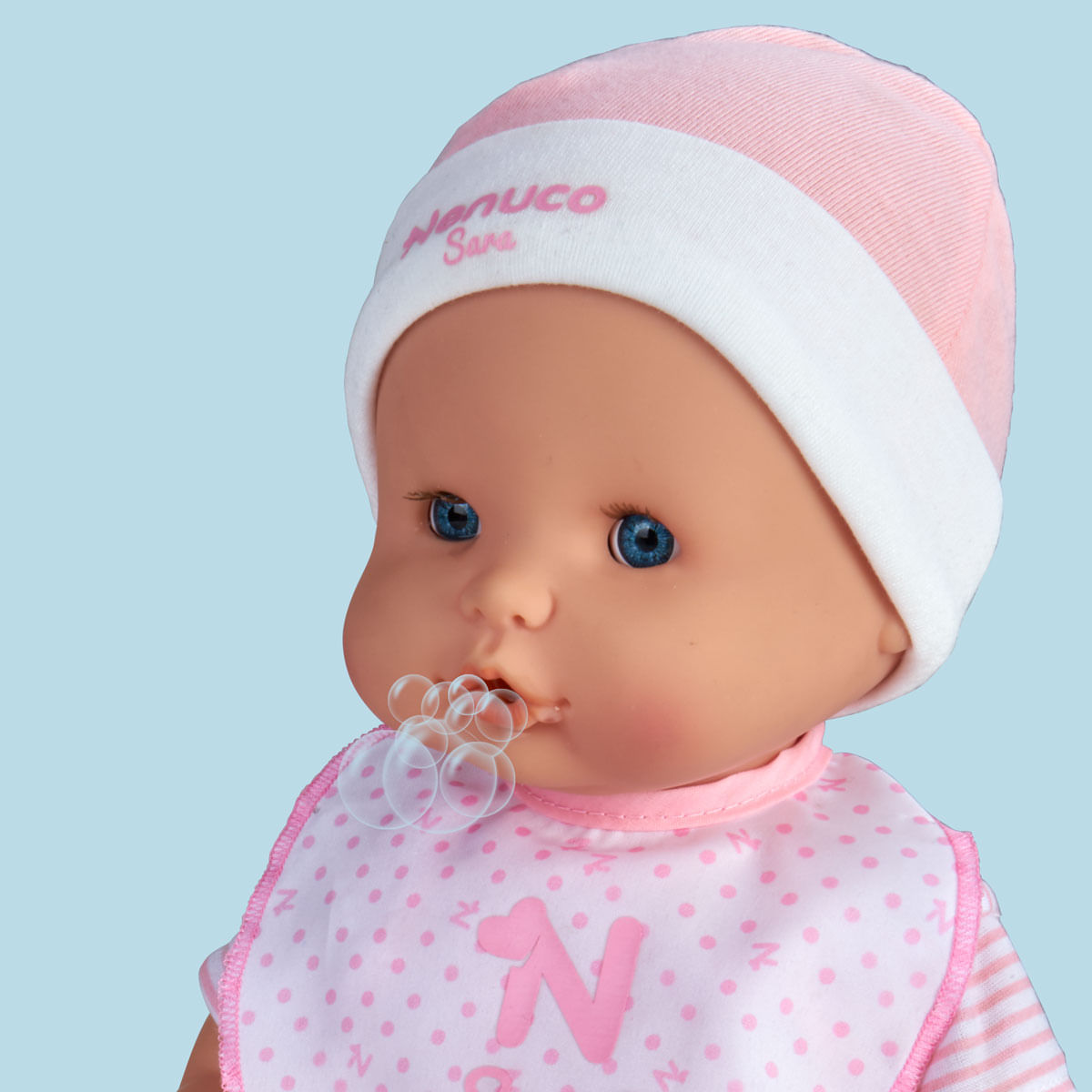 Una muñeca con ojos azules, con gorro y babero rosa y blanco. Salen burbujas de su boca. El fondo es azul claro.