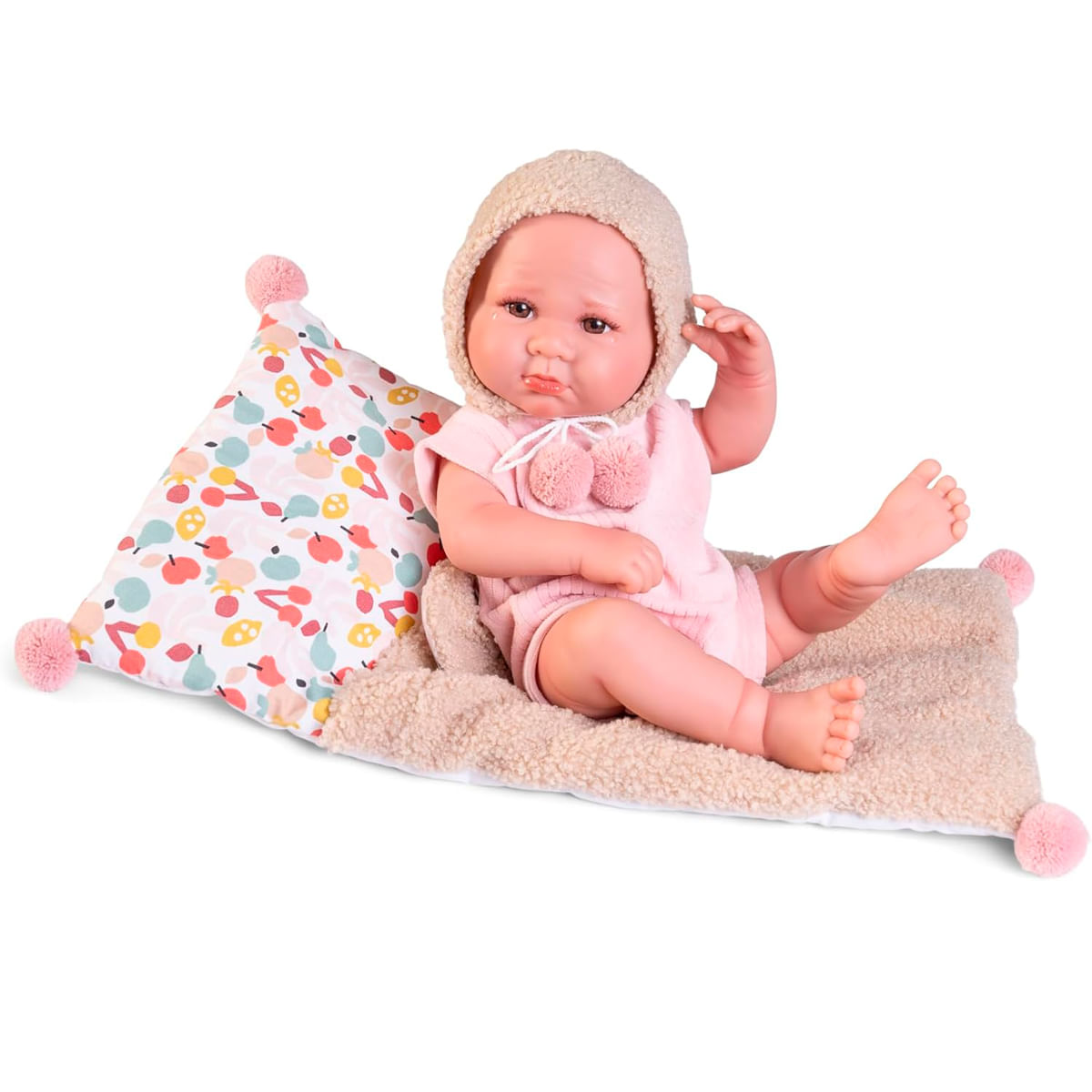 Una muñeca bebé con un atuendo y sombrero rosa está sentada en una manta con una almohada. La almohada tiene un patrón de frutas colorido.