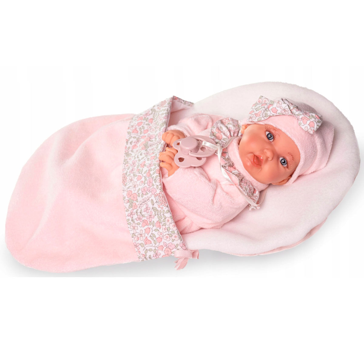 Una muñeca bebé con un traje y gorro rosa, con un lazo. Está acostada sobre una manta rosa y sostiene un chupete.