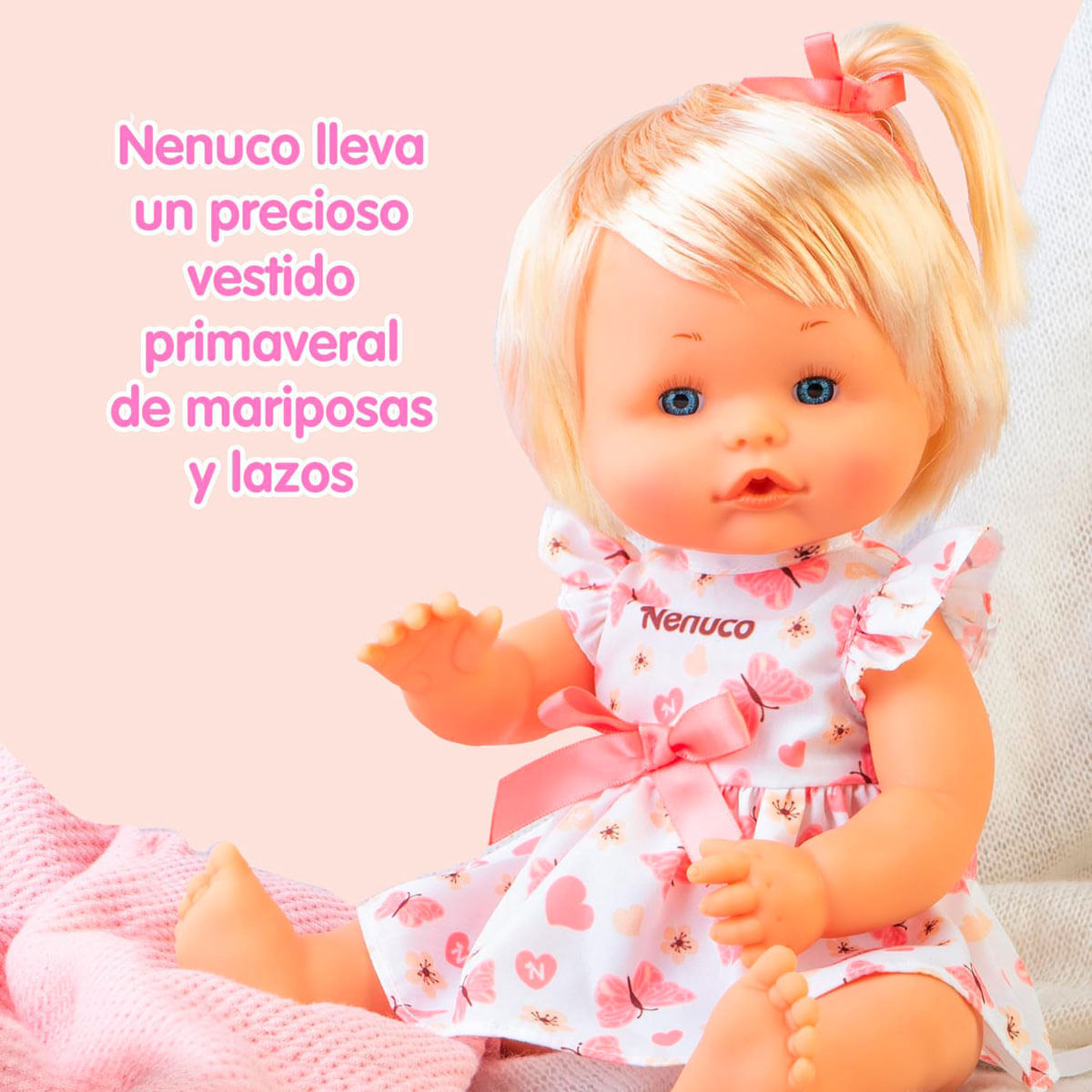 Una muñeca con pelo rubio y ojos azules lleva un vestido de mariposas. Lazo rosa en el pelo. El fondo es de color rosa claro.