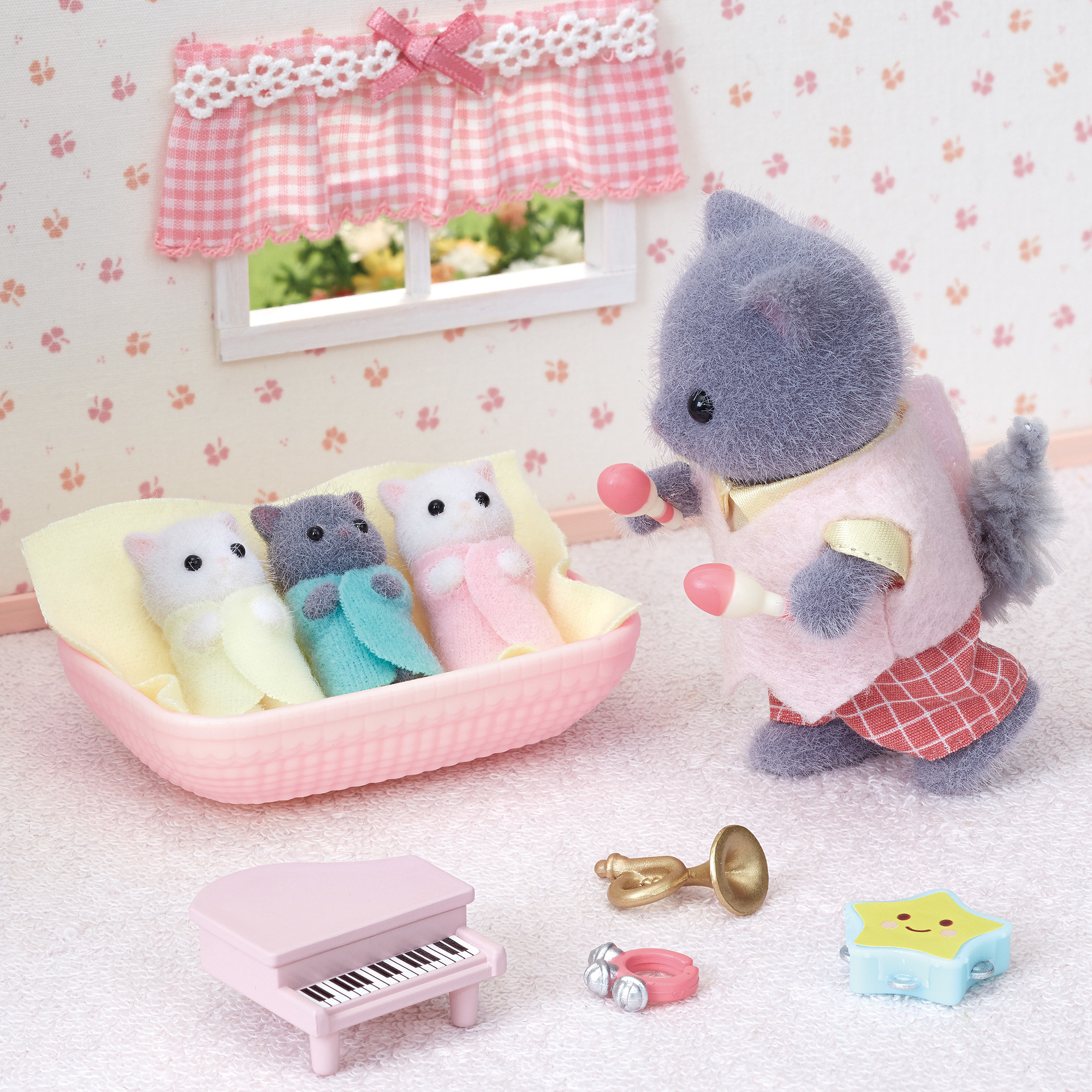 Un gato gris alimenta a tres gatitos de juguete en una cesta. Hay un piano, una trompeta y un juguete en forma de estrella.