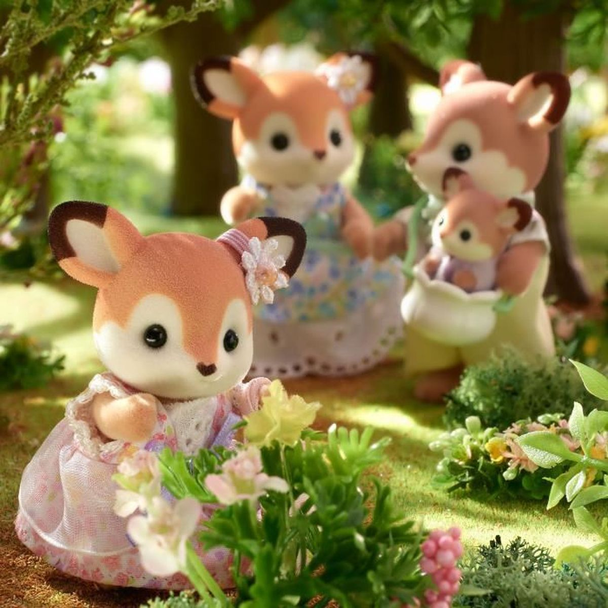 Vier Fuchsstatuen in einem Garten. Eine in einem rosa Kleid, andere in Kleidern, eine hält ein Baby in einem Beutel. Grünes Gras und Blumen.