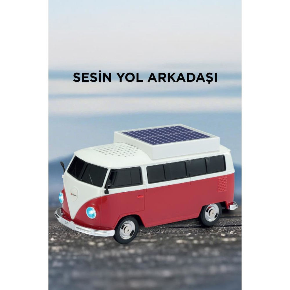 Üstünde güneş paneli olan kırmızı ve beyaz bir oyuncak otobüs. Farları ve hoparlörü var. Arka plan bulanık bir okyanus.