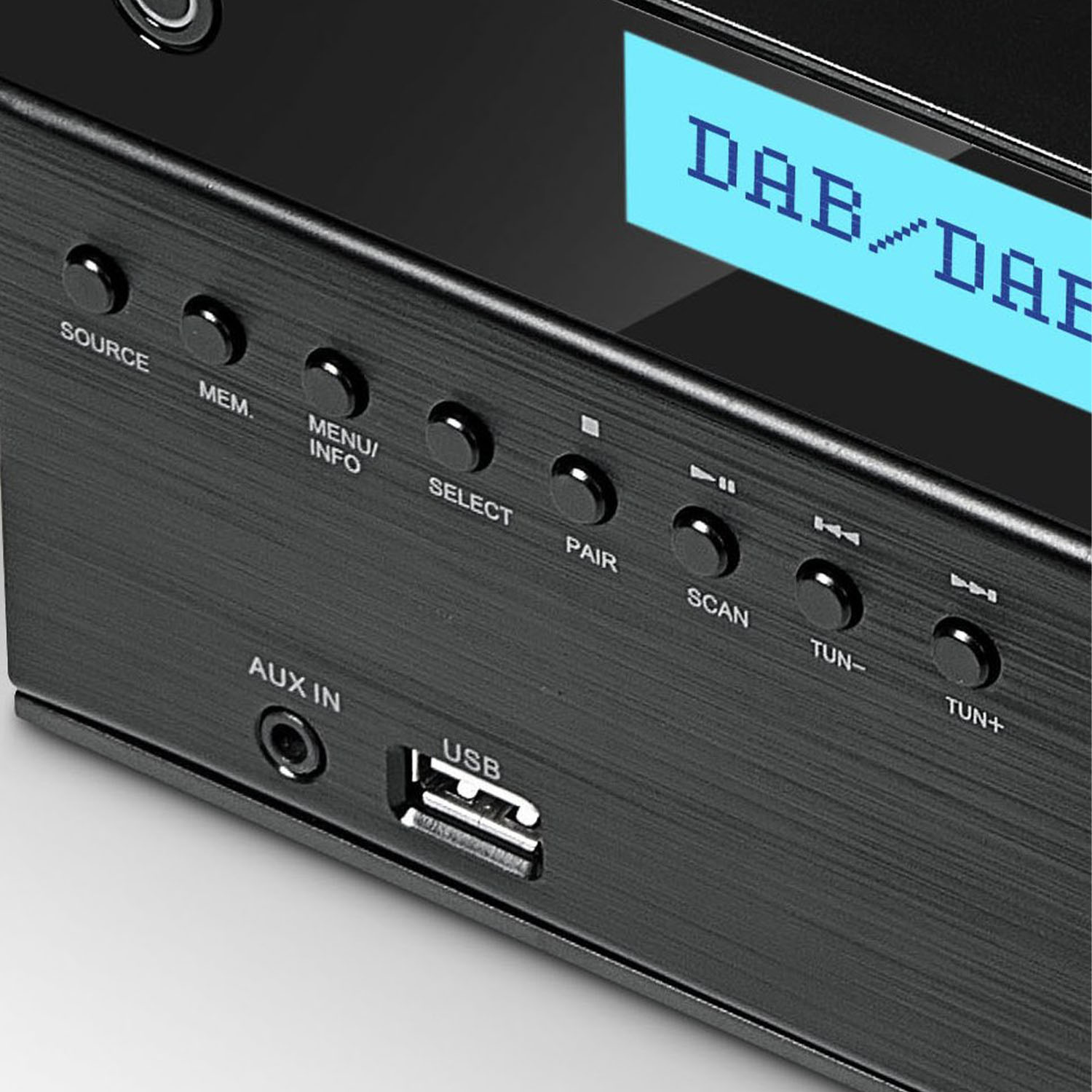 Schwarzes Audiogerät mit Knöpfen wie Source, Menu, Pair, Scan, Tun- und Tun+. Es hat einen Bildschirm mit 'DAB'. USB- und AUX-Anschlüsse sind sichtbar.