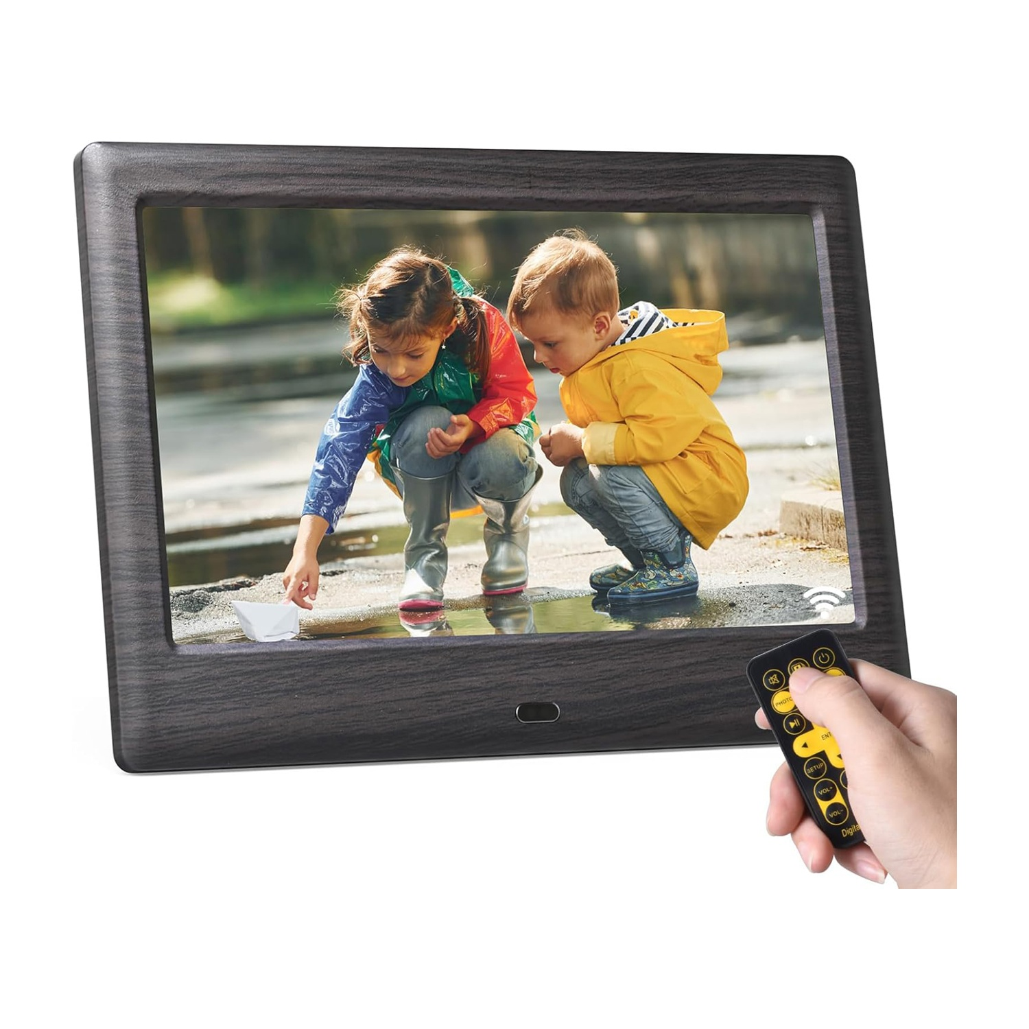 Una cornice digitale mostra due bambini che giocano con una barchetta di carta. Una mano tiene un telecomando.
