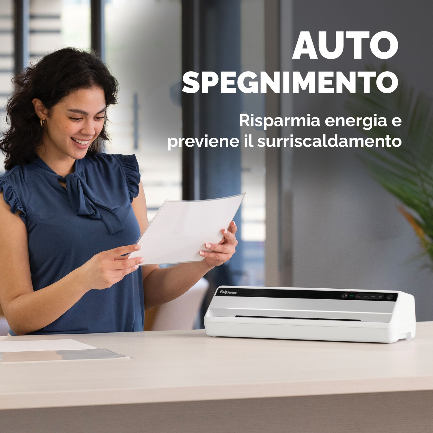 Kobieta uśmiecha się, trzymając papier. Biała laminarka na biurku. Tekst: AUTO SPEGNIMENTO, oszczędza energię i zapobiega przegrzaniu.