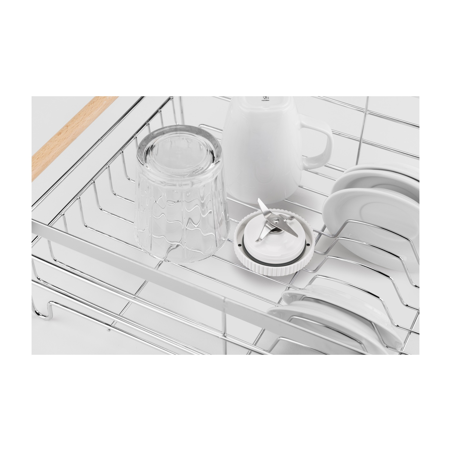 Ein Geschirrkorb enthält ein Glas, einen weißen Becher, ein Blenderteil und weiße Teller. Der Korb ist aus Metall und der Hintergrund ist weiß.