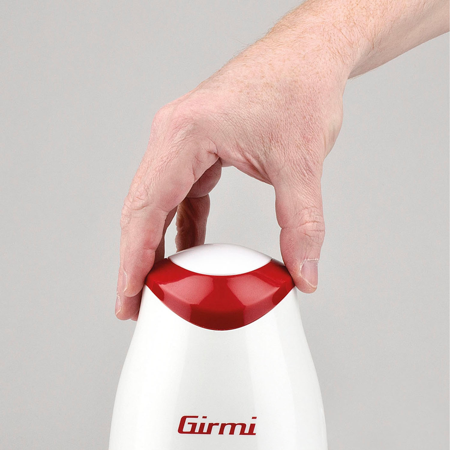 Eine Hand hält ein weiß-rotes Girmi-Gerät. Die Hand ist über dem Gerät positioniert, die Finger um die Oberseite gelegt.