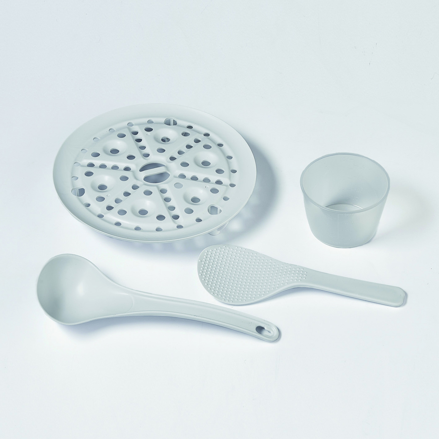 Un juego de utensilios de cocina grises claros sobre una superficie blanca, que incluye una vaporera, un cucharón, una cuchara de arroz y una taza medidora.