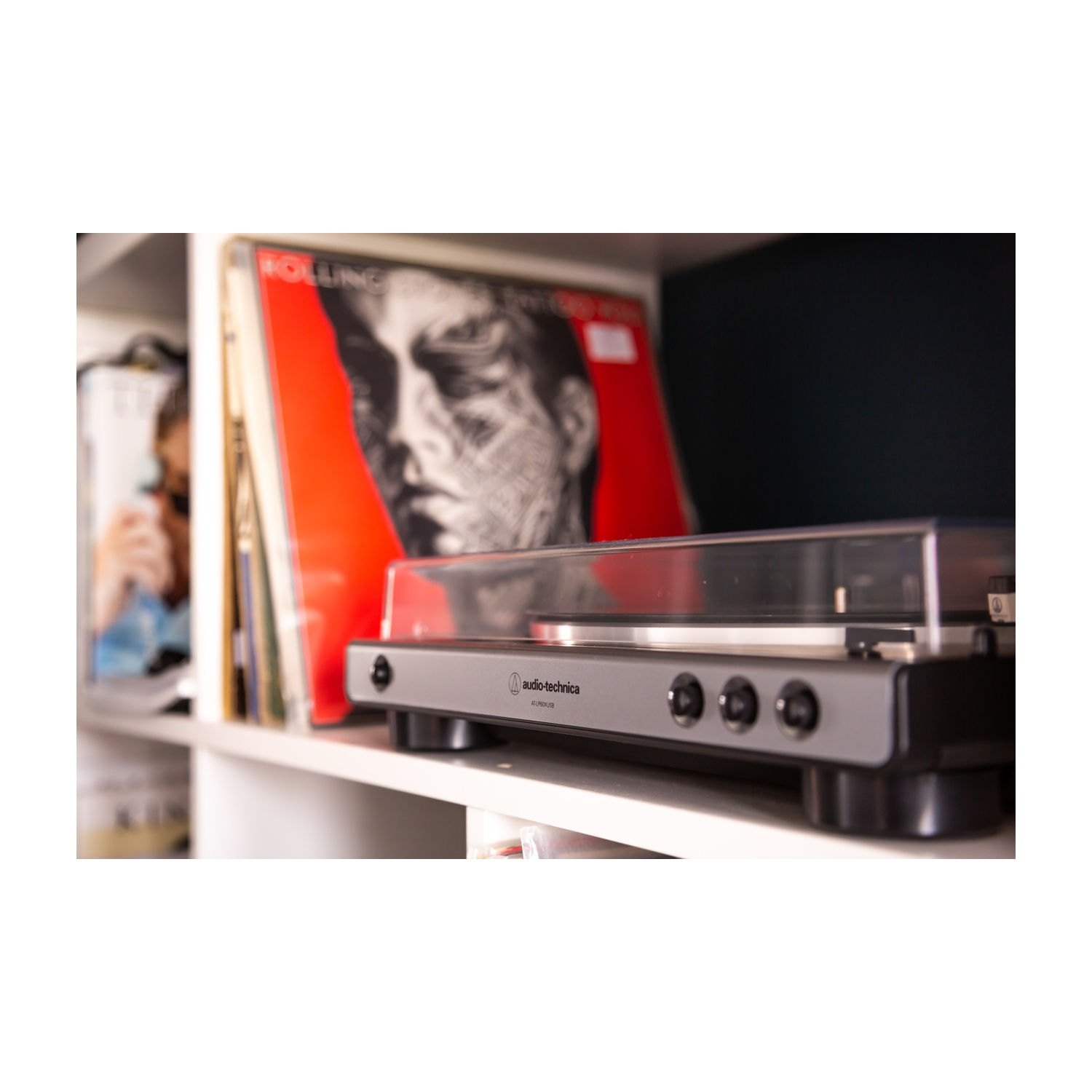 Gramofon na półce z płytami winylowymi. Osoba lekko widoczna w tle. Widoczny album Rolling Stones.