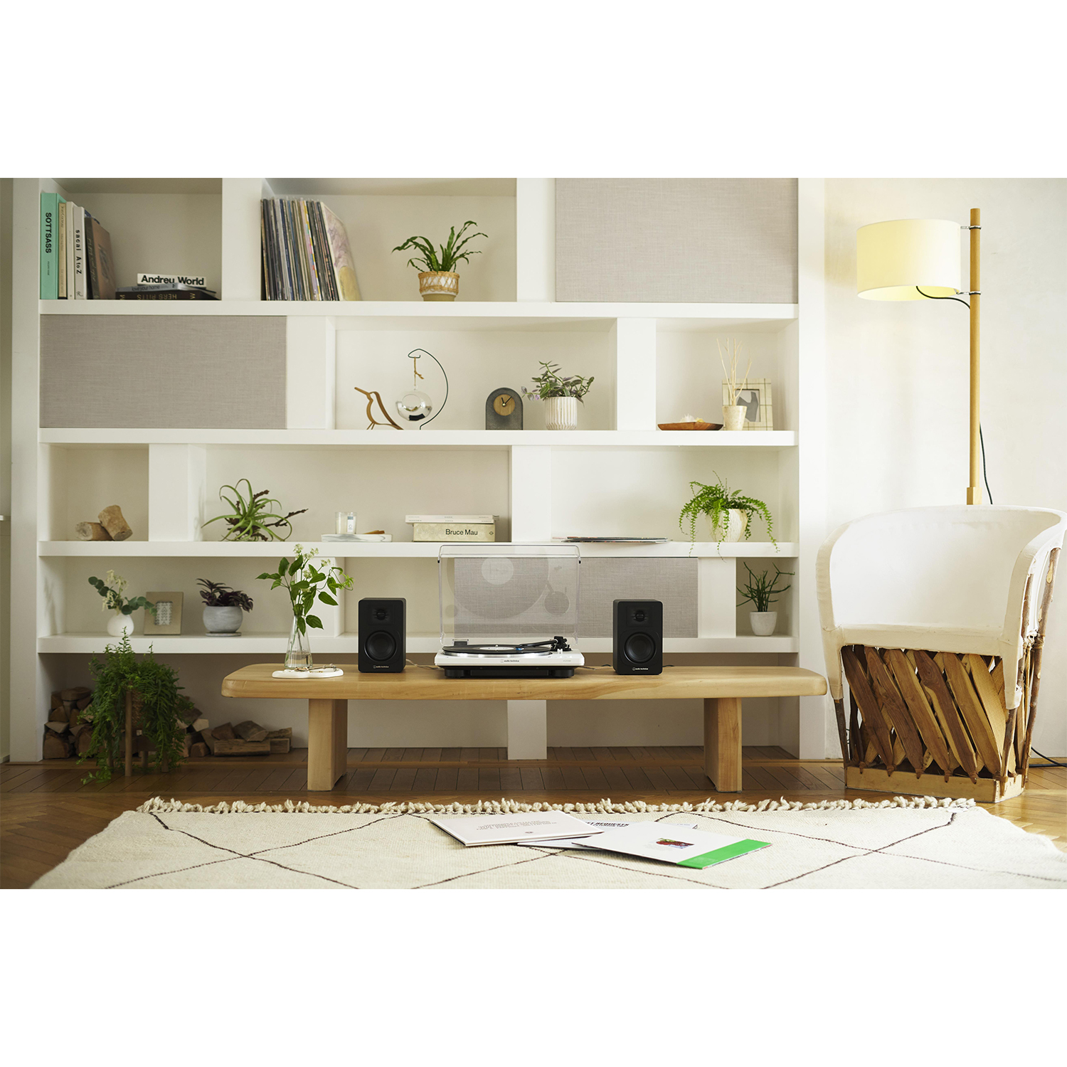 Nowoczesny salon z gramofonem, głośnikami i białym krzesłem. Regały i rośliny w tle.