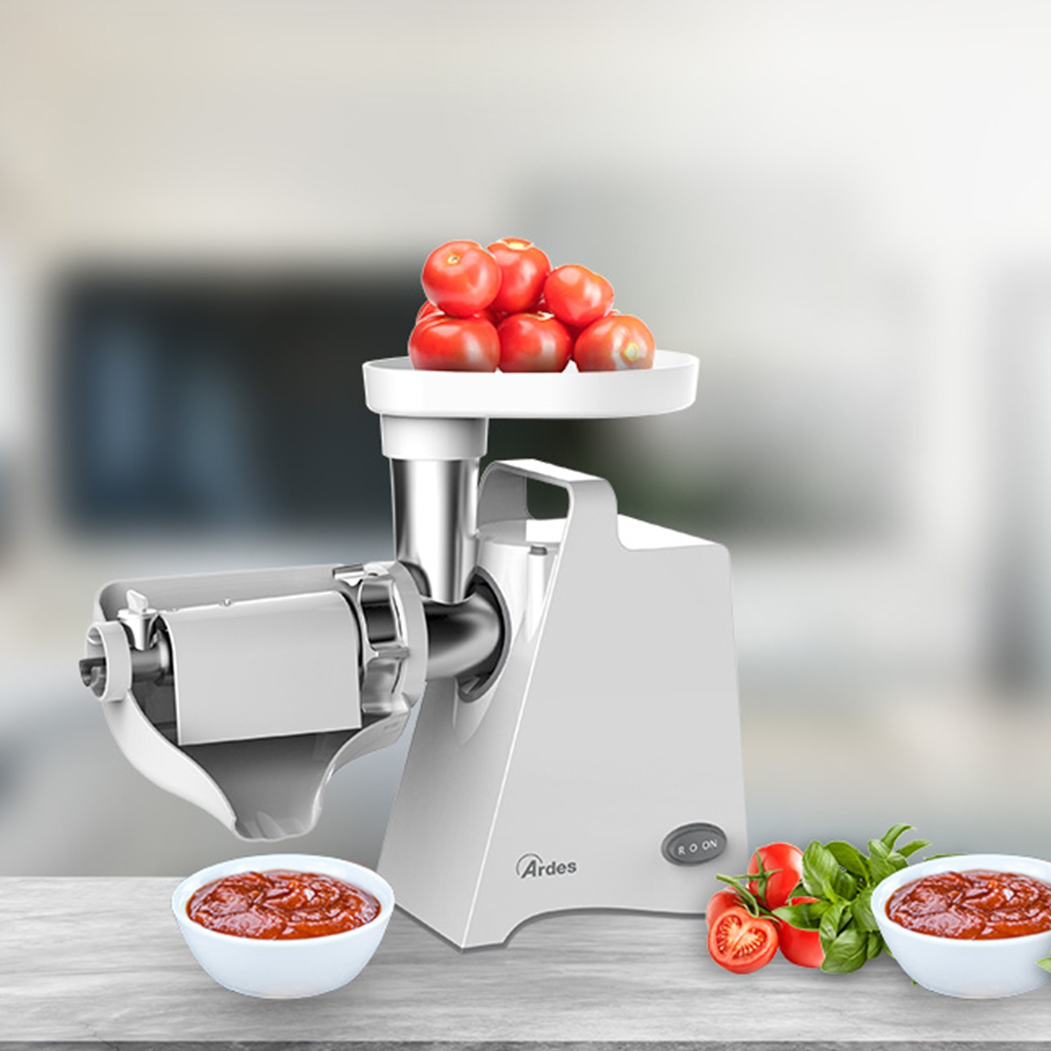 Una máquina para moler tomates blanca con tomates encima, dos cuencos de salsa y tomates y albahaca sobre madera.