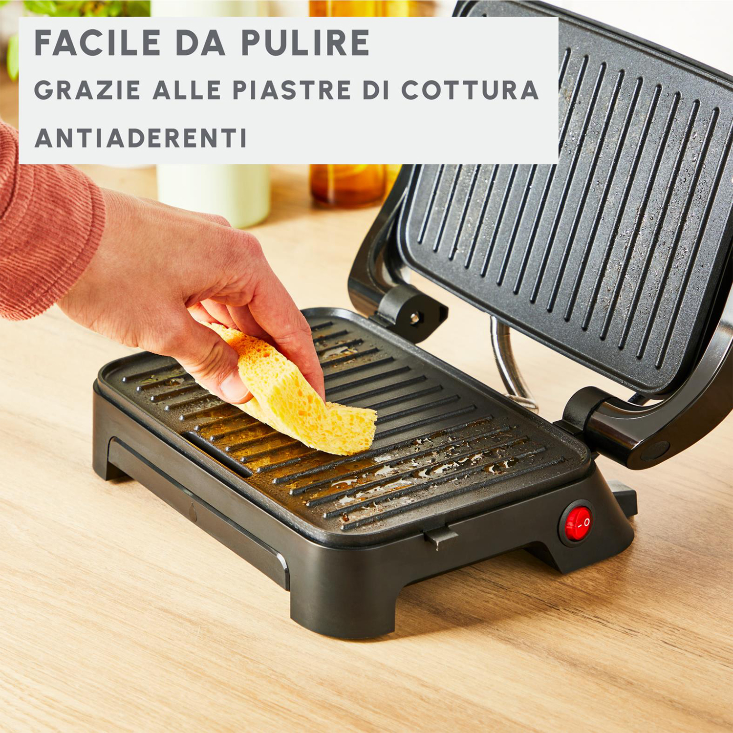 Eine Hand legt ein Brotstück auf einen schwarzen Grill. Der Grill ist offen und hat Antihaft-Kochplatten.