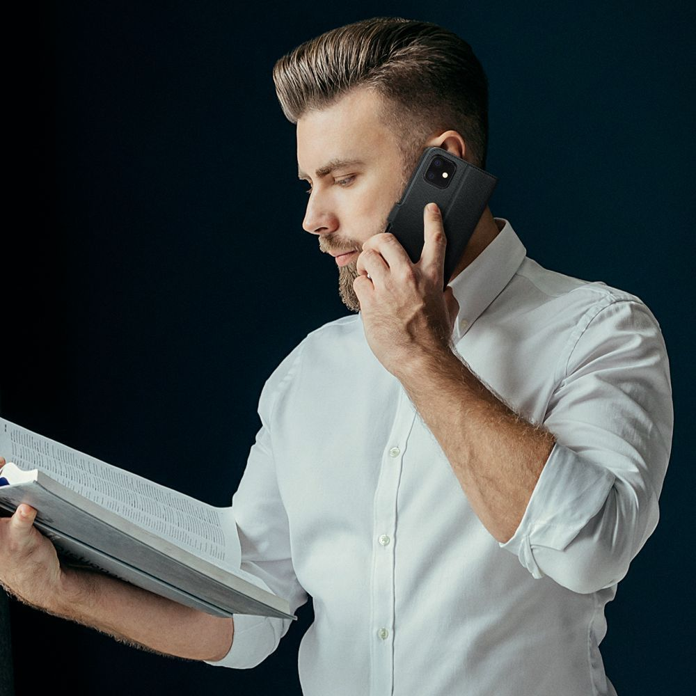 Ein Mann im weißen Hemd telefoniert mit einer schwarzen Handyhülle und liest ein Buch. Dunkelblauer Hintergrund.