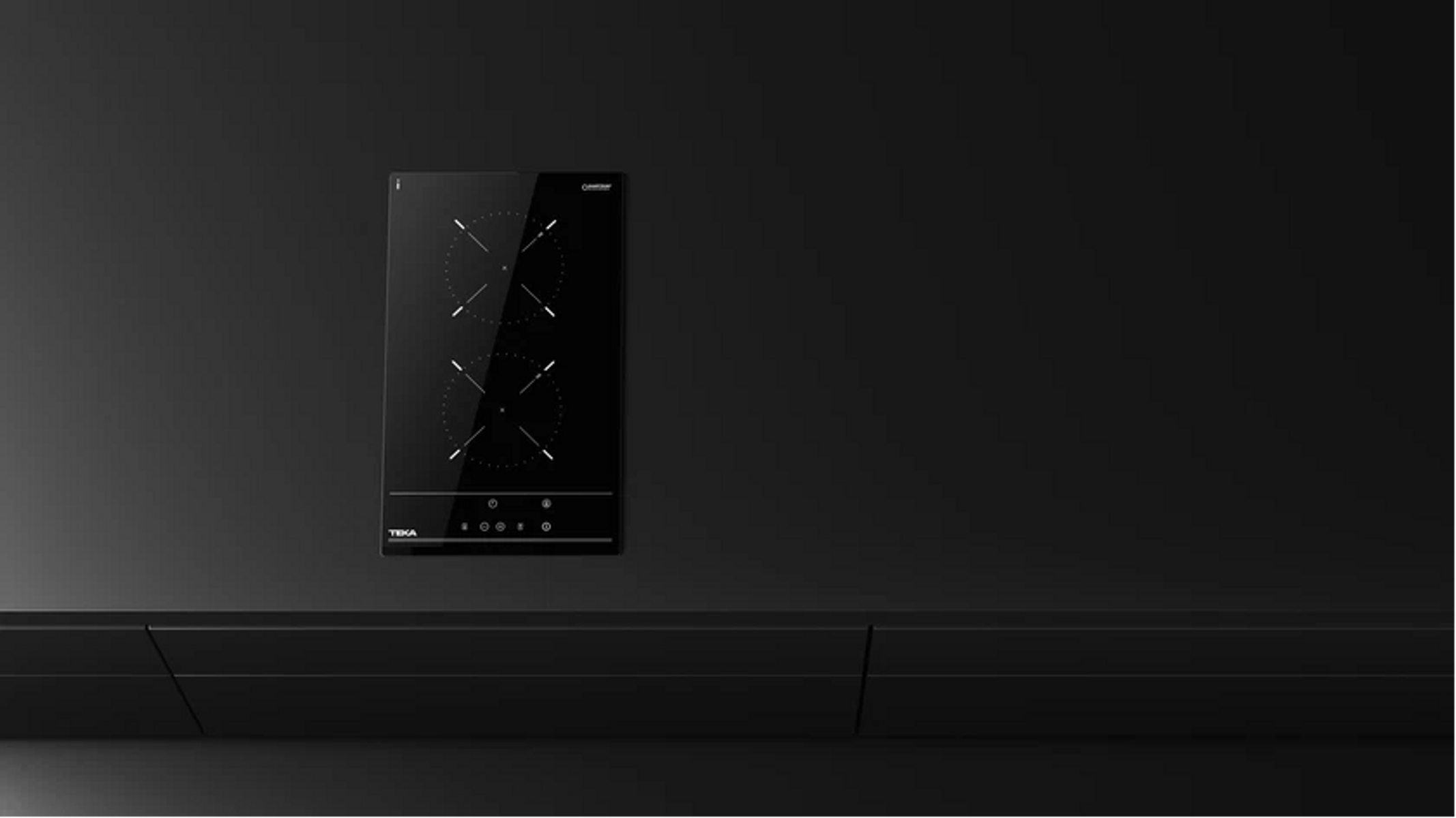 Placa de inducción Teka negra con dos quemadores. Montada sobre una superficie negra. El fondo también es negro.