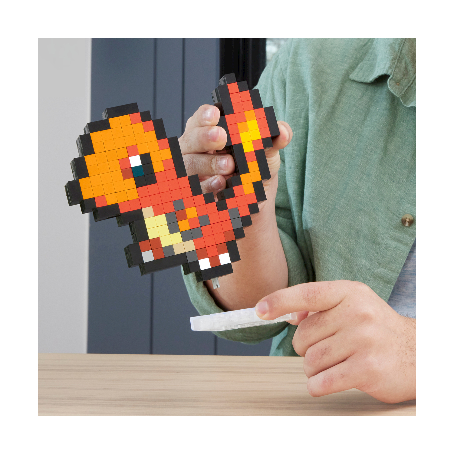 Une personne tient une figurine pixelisée de Salamèche. La figurine est orange, jaune et noire. Une main pointe vers une pièce blanche.
